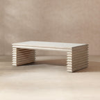 Whitewashed reclaimed pine coffee table featuring a geometric, stacked-wood waterfall base in a natural finish.