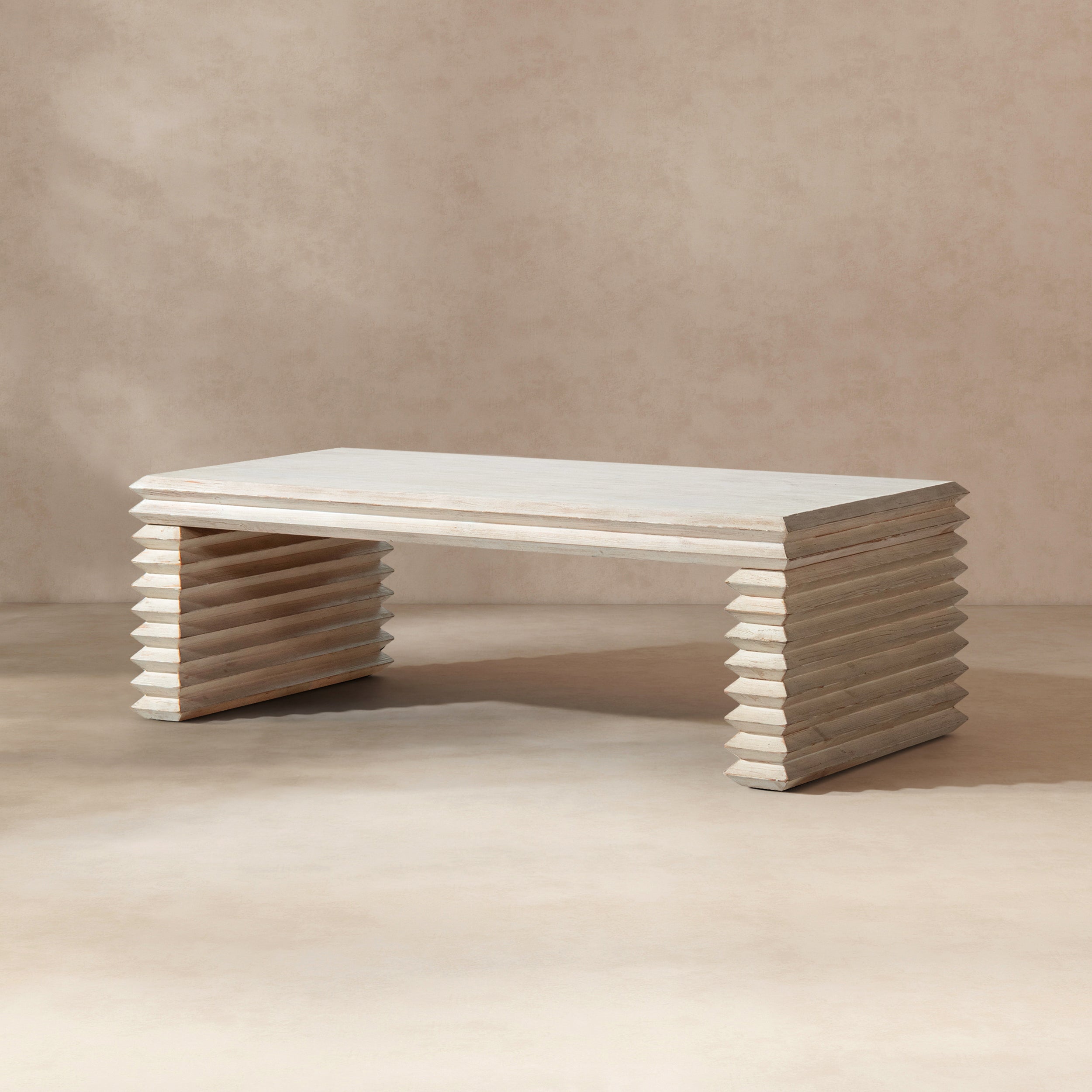 Whitewashed reclaimed pine coffee table featuring a geometric, stacked-wood waterfall base in a natural finish.