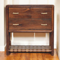 Wooden dresser with three drawers and a woven shelf on a wooden floor.