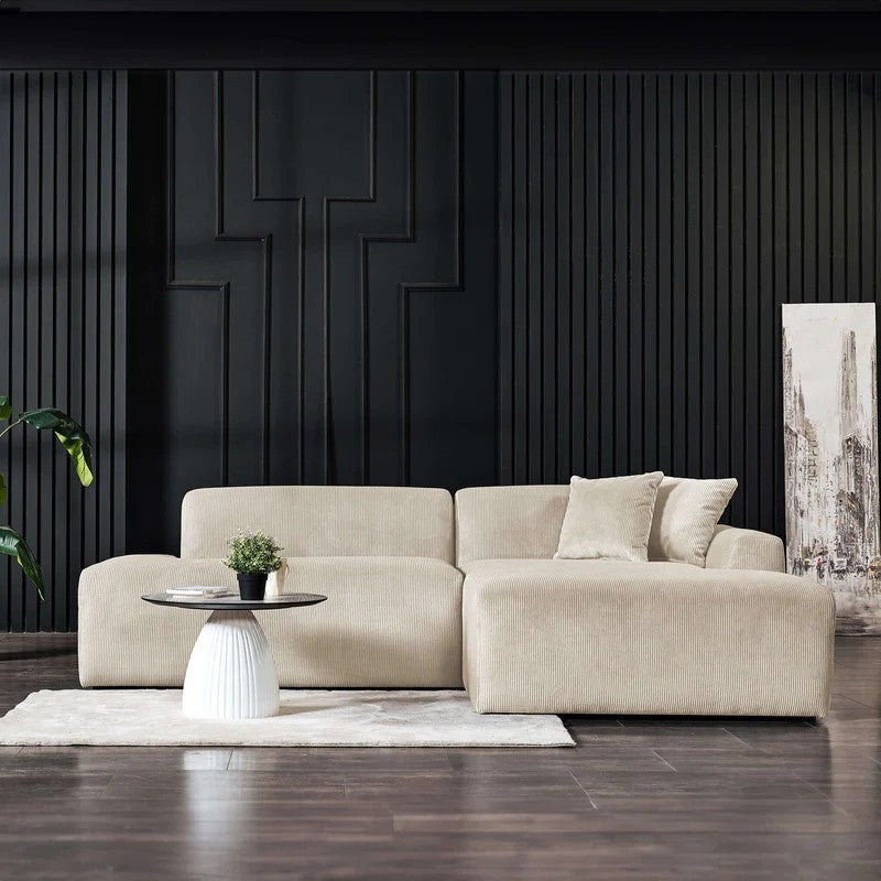 Cream corduroy right-facing sectional sofa with a modern, low-profile design set against a black paneled wall.