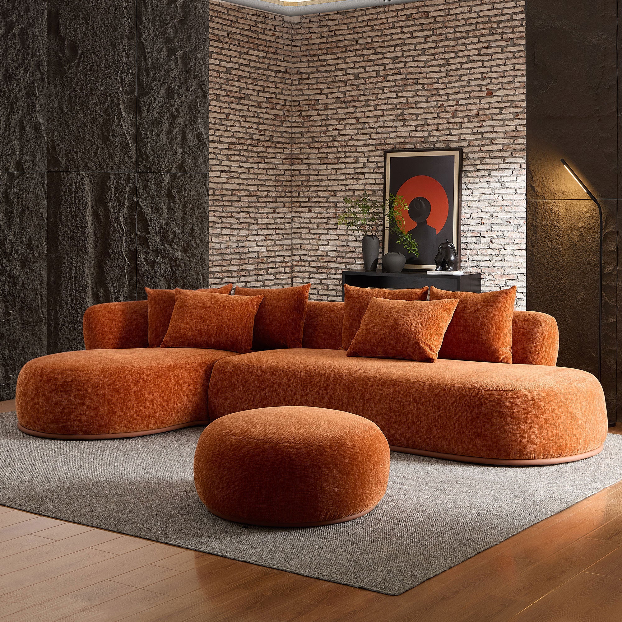 Orange oversized L-shape sectional sofa with ottoman in a dark-toned room, highlighting its bold color and cozy seating.