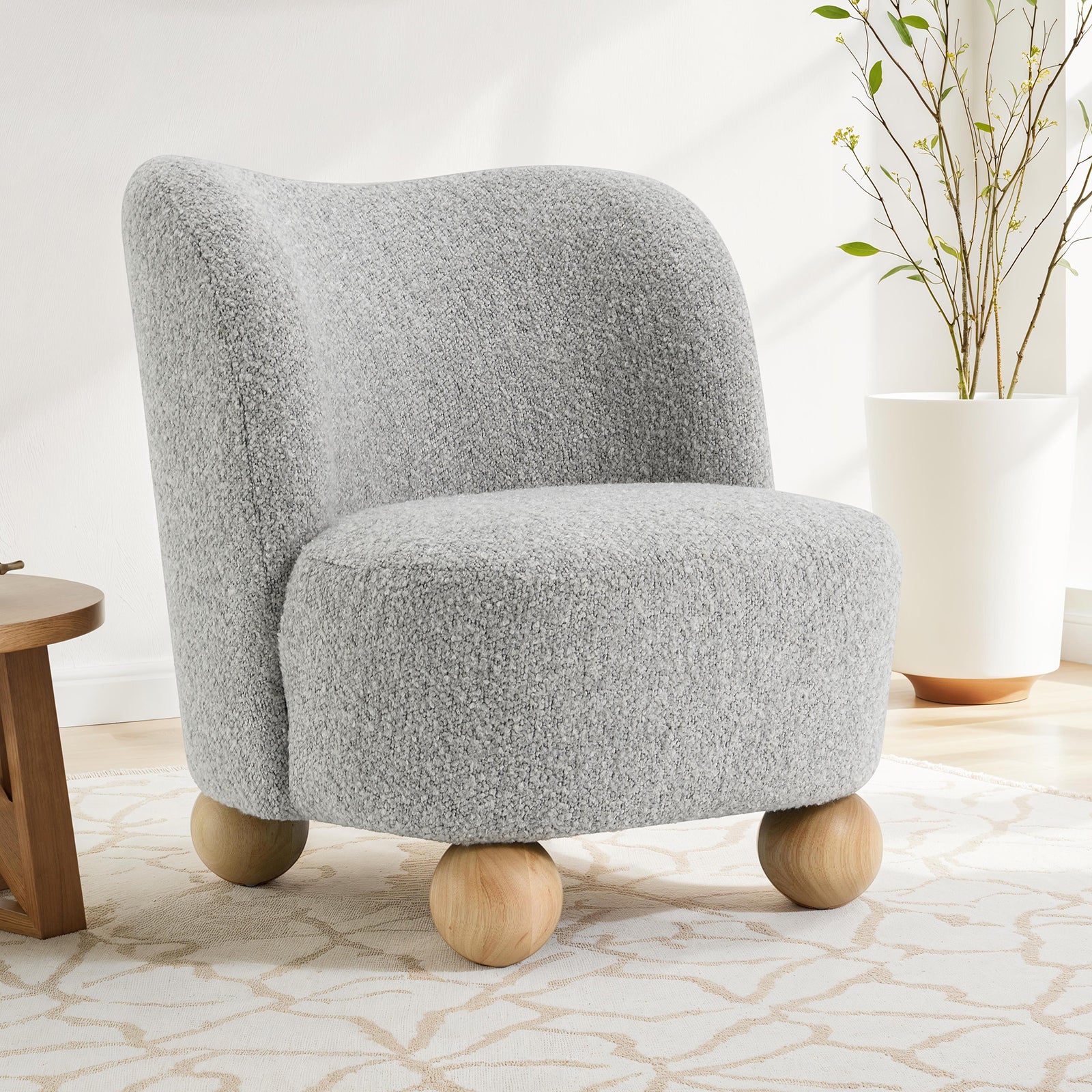 Modern gray upholstered accent chair in boucle fabric with curved backrest and wooden ball legs, perfect for stylish interiors.