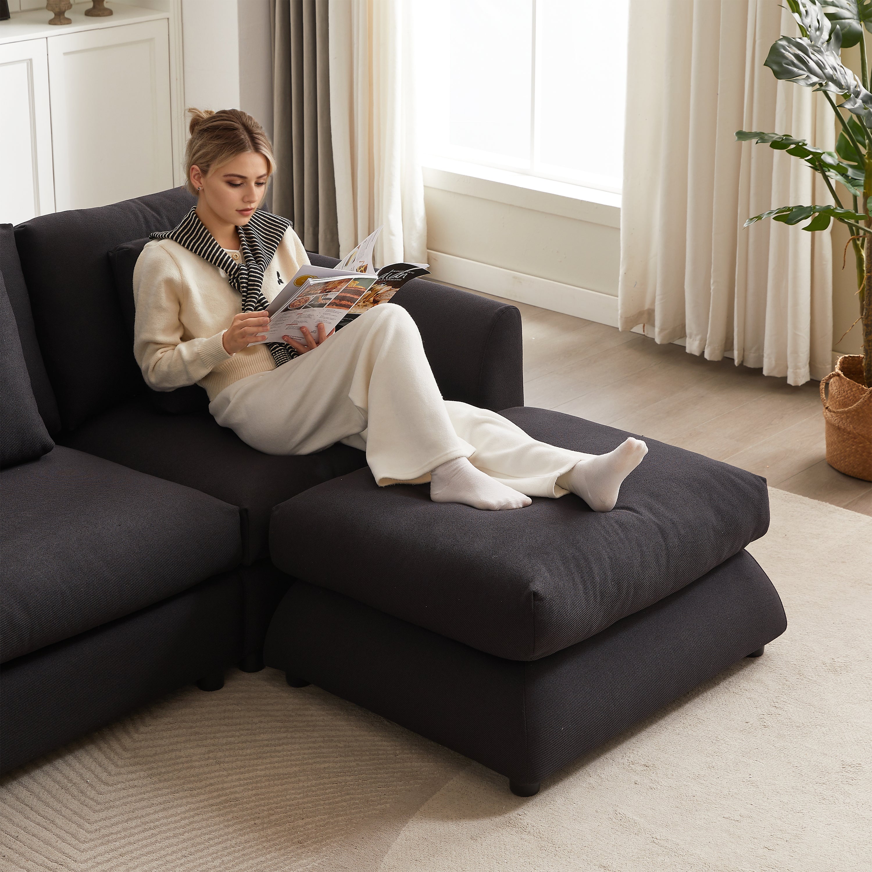 Woman relaxing on L-shaped modular sofa with ottoman, showcasing comfort and spacious seating for reading or lounging.