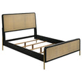 Black queen bed frame with natural woven rattan panels, rounded corners, and slim metallic gold legs on a white background.