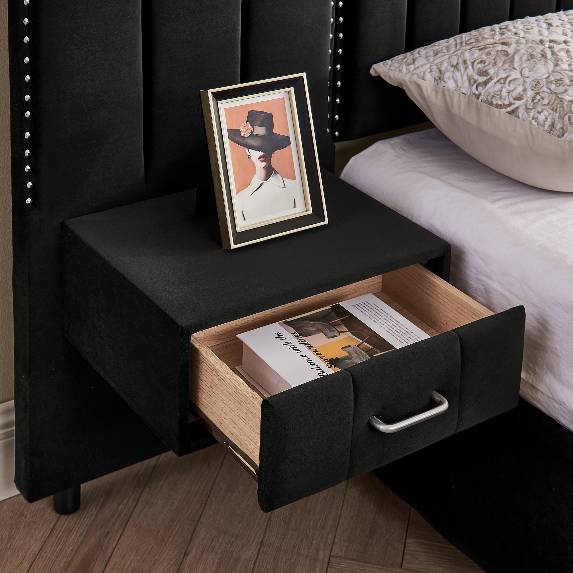 Open drawer of built-in bedside table on velvet bed frame, showing storage space for books and personal items.