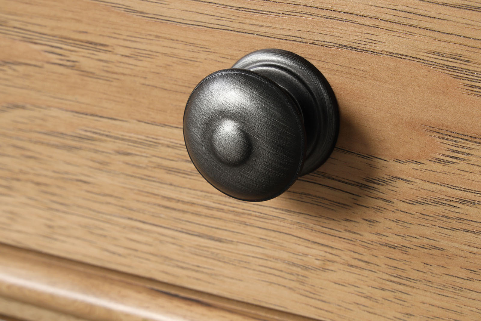 Close-up of black metal knob on Farmhouse Oak Nightstand. Matte finish complements rustic oak wood grain.
