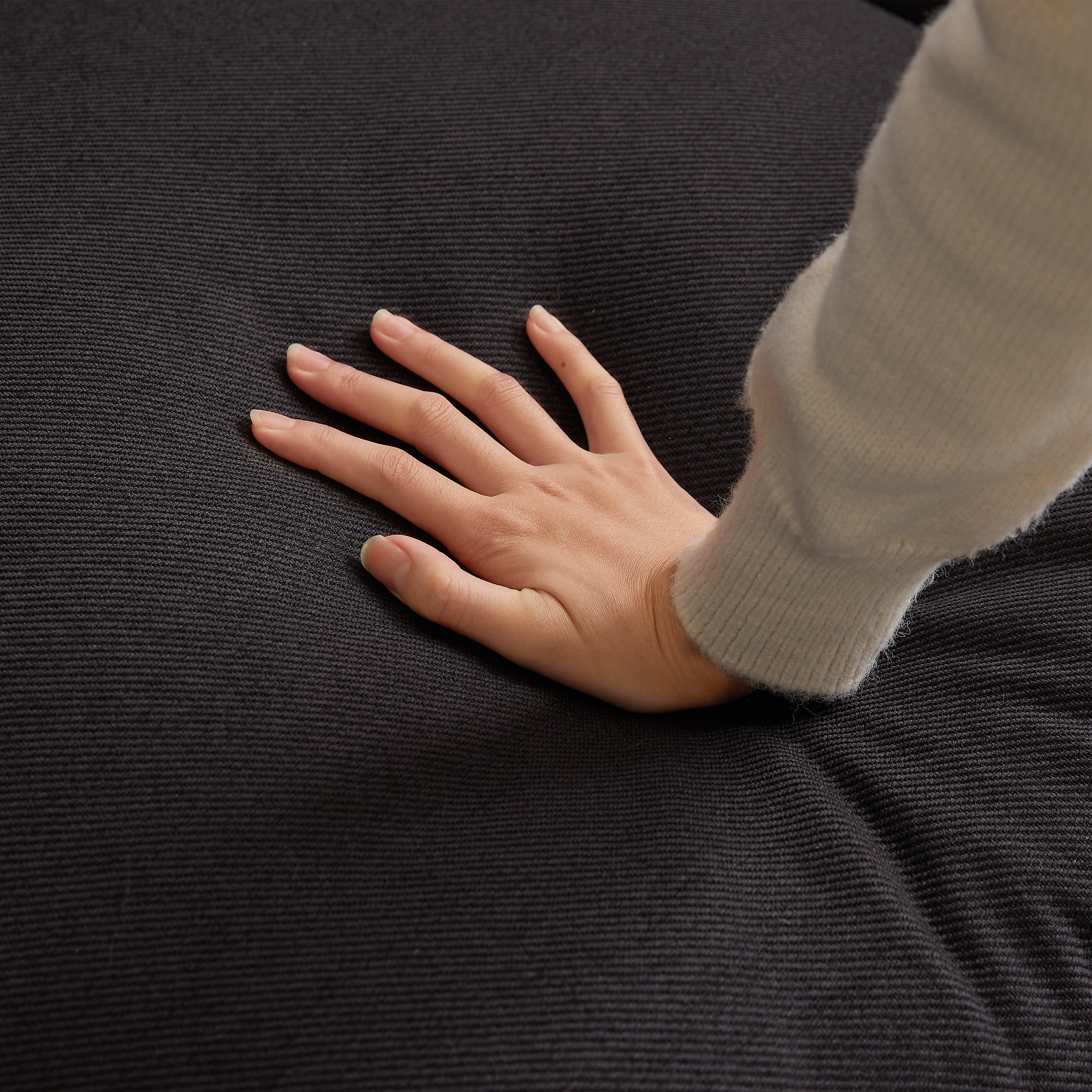 Hand pressing into cushion of modular L-shaped sofa, demonstrating the soft and supportive foam padding.