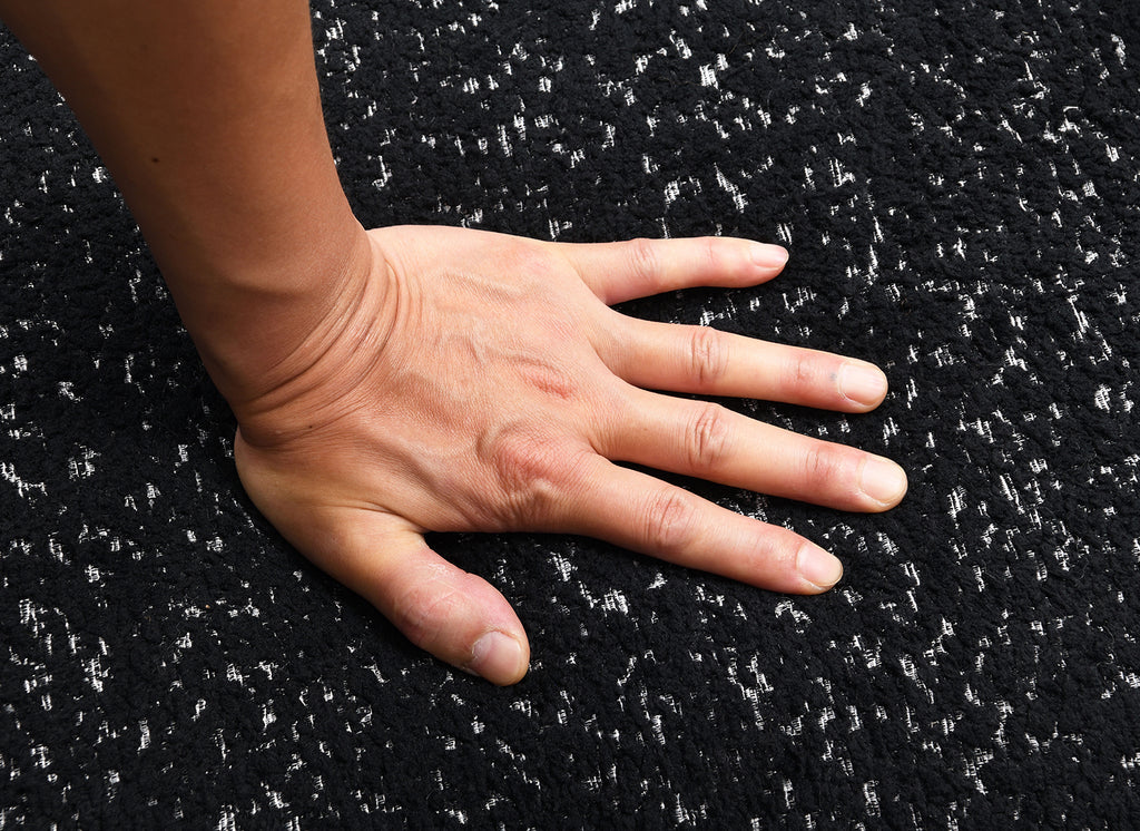 Hand pressing into high-density foam seat of black swivel chair. Demonstrates plush comfort and premium cushioning.