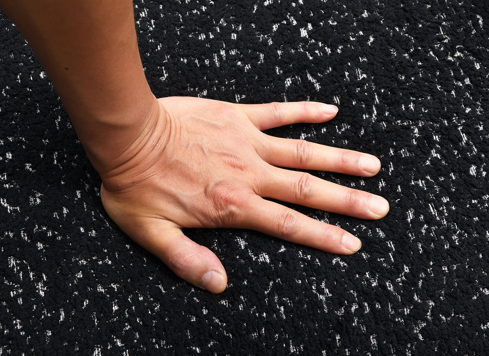 Hand pressing into high-density foam seat of black swivel chair. Demonstrates plush comfort and premium cushioning.
