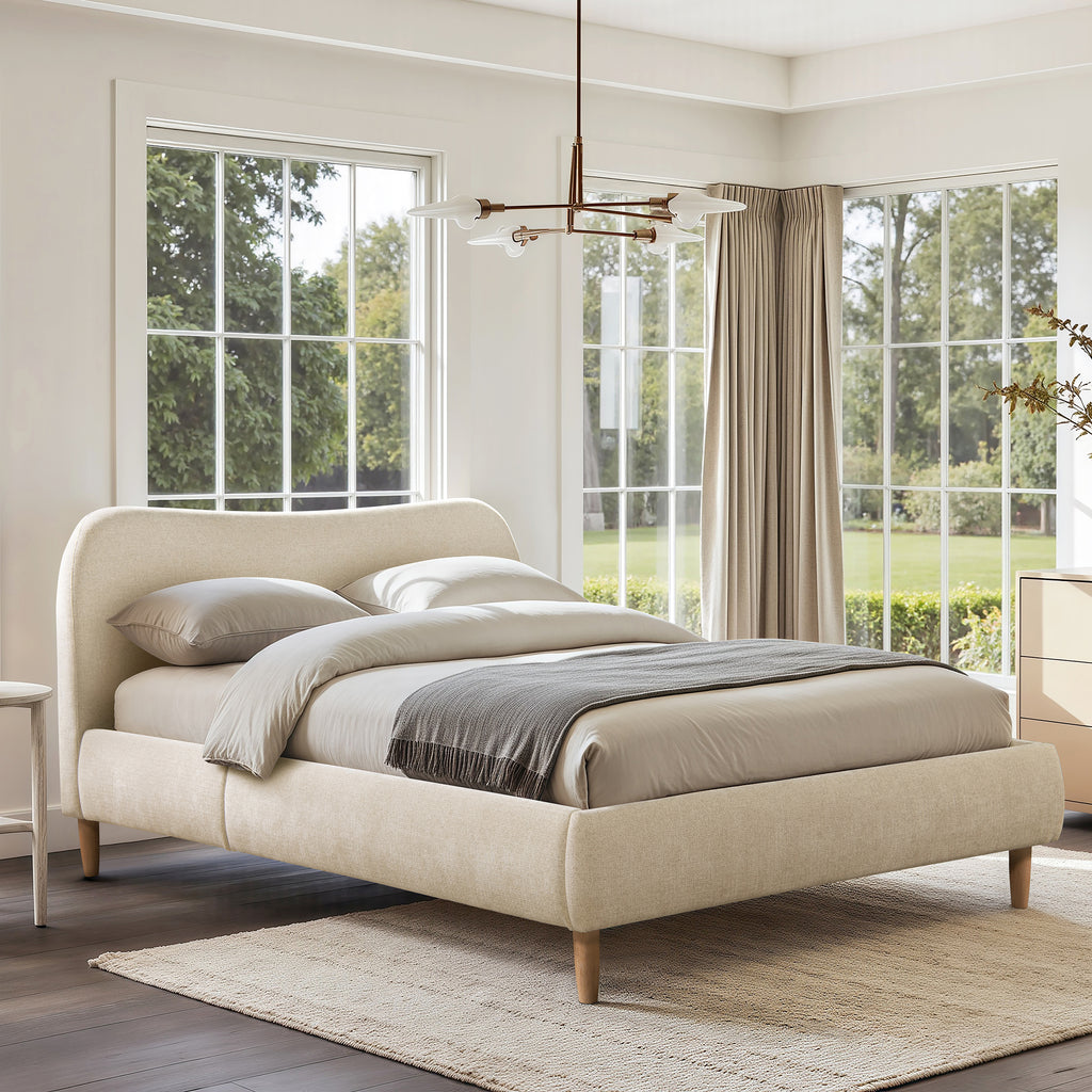 Platform Bed - Beige Upholstered Curved Headboard placed in a sunlit room with large windows, showcasing its soft chenille fabric and wooden legs.