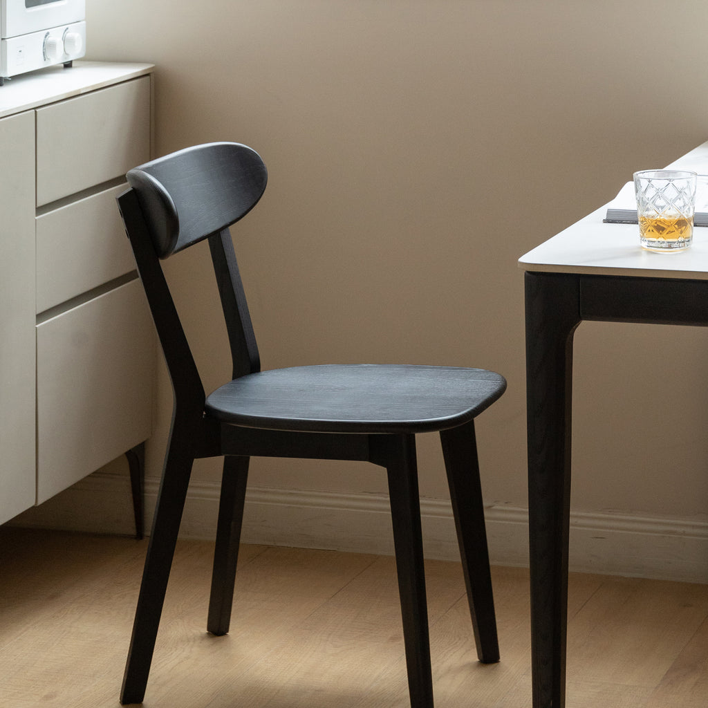 Black Solid Oak Dining Chair placed beside a white dining table in a modern kitchen setting with natural light.