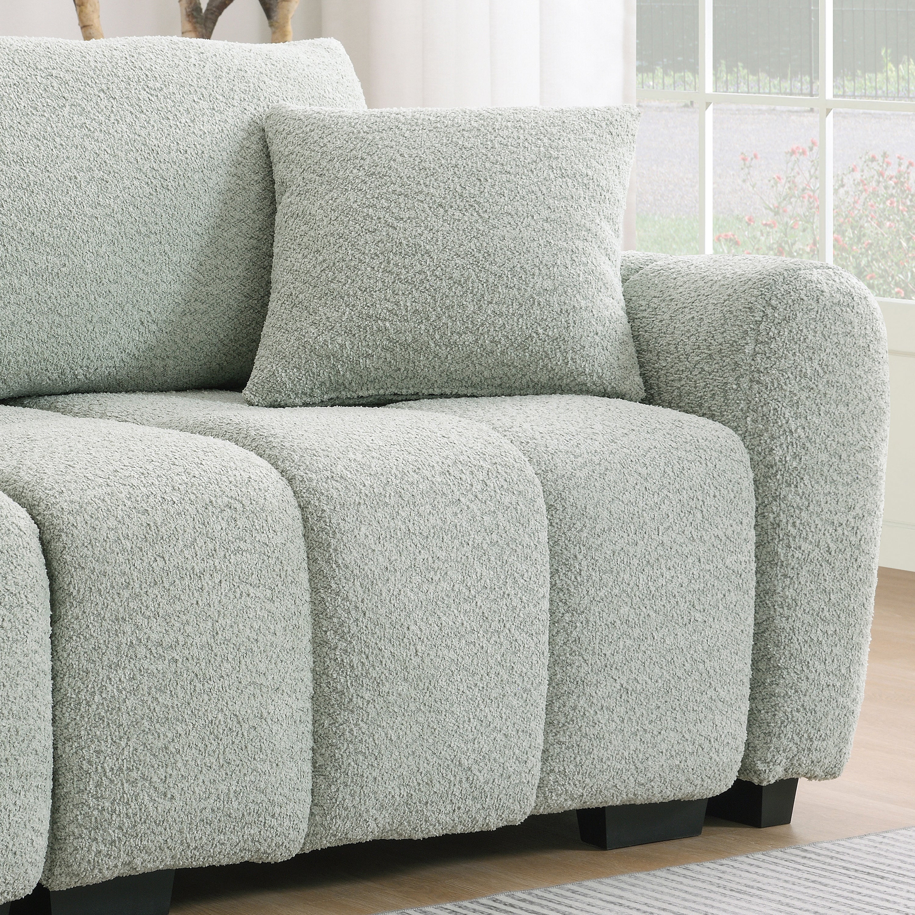 Armrest and cushion detail of modular sectional sofa with ottoman, showcasing thick padding and soft boucle upholstery.