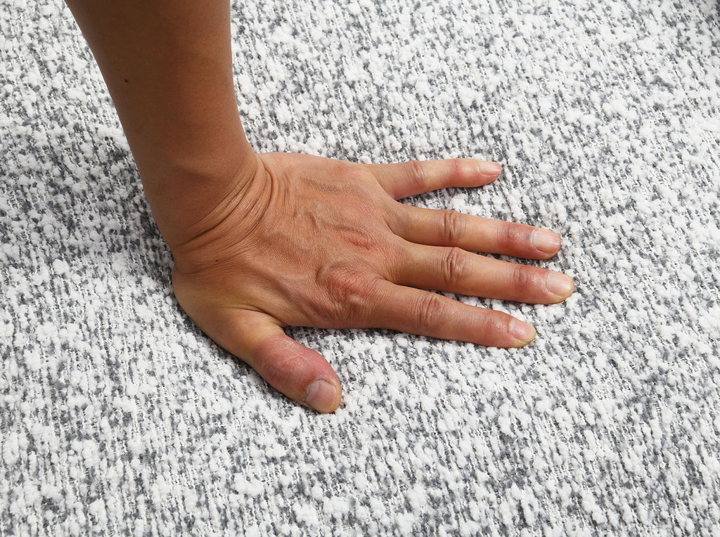 Hand pressing on the soft, high-density foam seat of the Contemporary Swivel Chair in gray, demonstrating its comfort and texture.