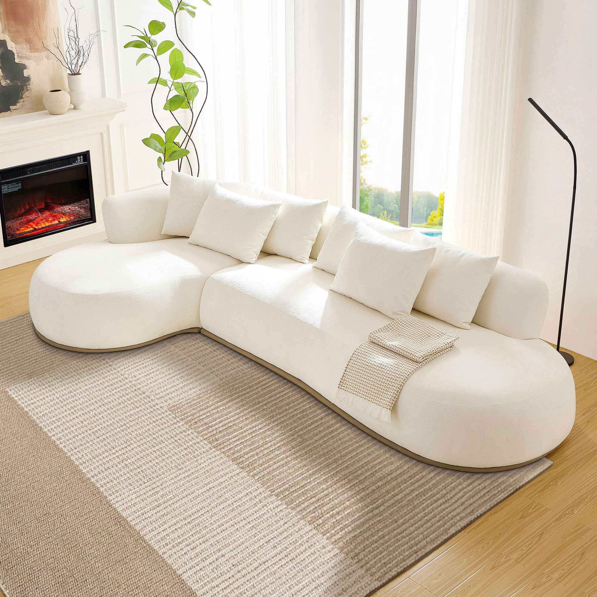 Modern Oversized L-Shape Sectional Sofa Beige with chaise lounge, placed near large windows and a fireplace, styled with throw pillows and blanket.