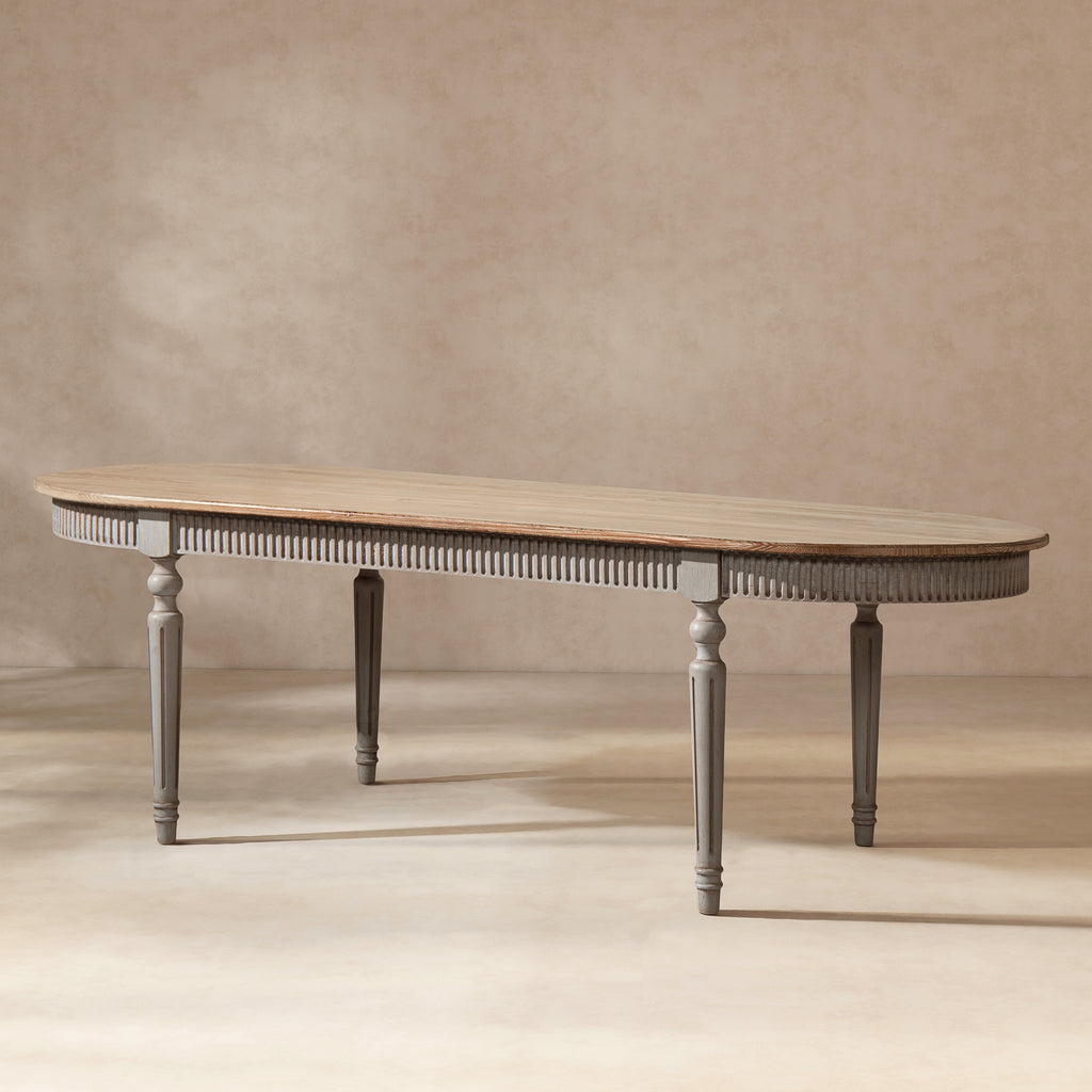 Oval reclaimed pine dining table with a natural wood top, antique blue-grey fluted apron, and elegant tapered legs.