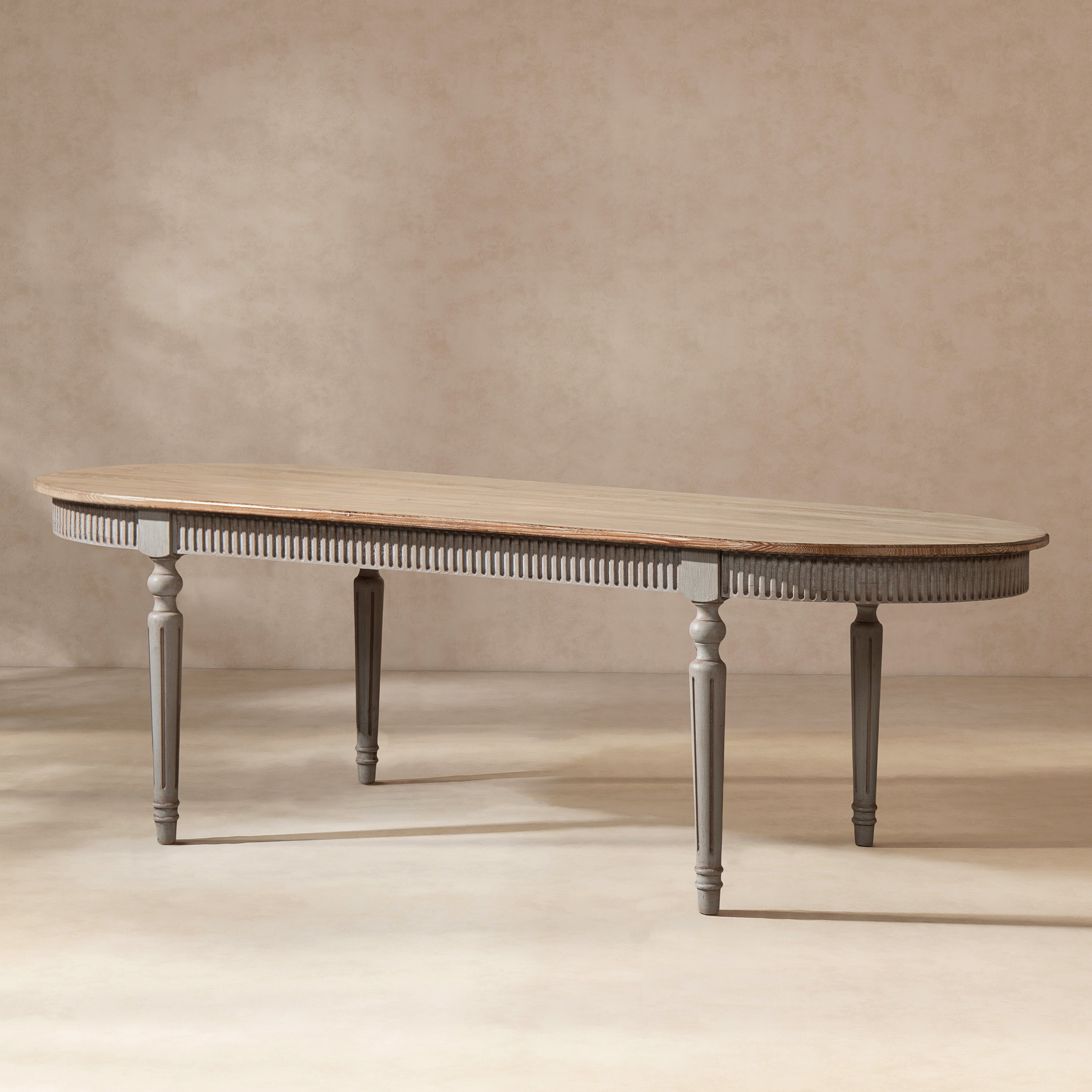Oval reclaimed pine dining table with a natural wood top, antique blue-grey fluted apron, and elegant tapered legs.