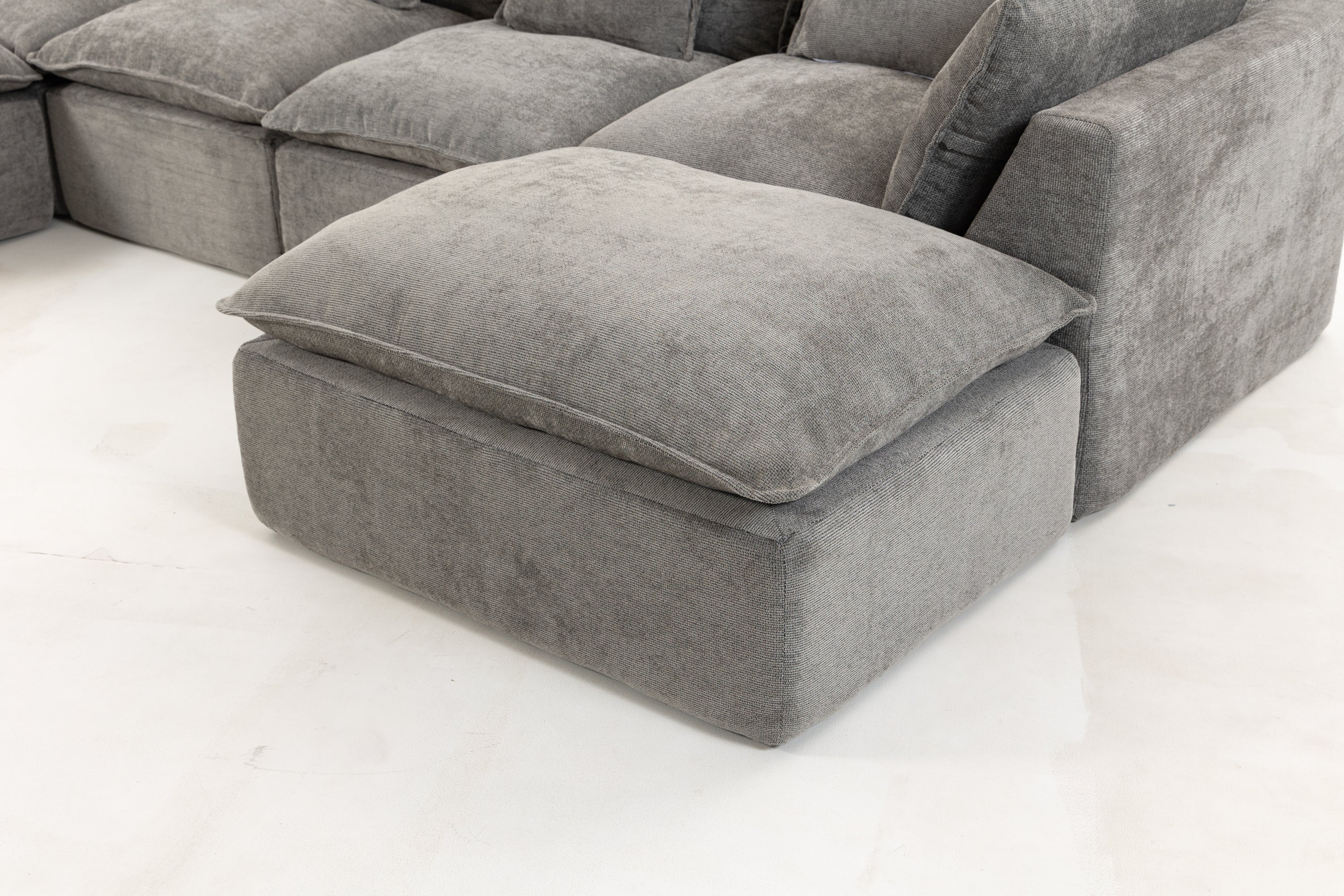 Detail of modular ottoman section from oversized sectional sofa in soft grey velvet, highlighting cloud-like cushion comfort.