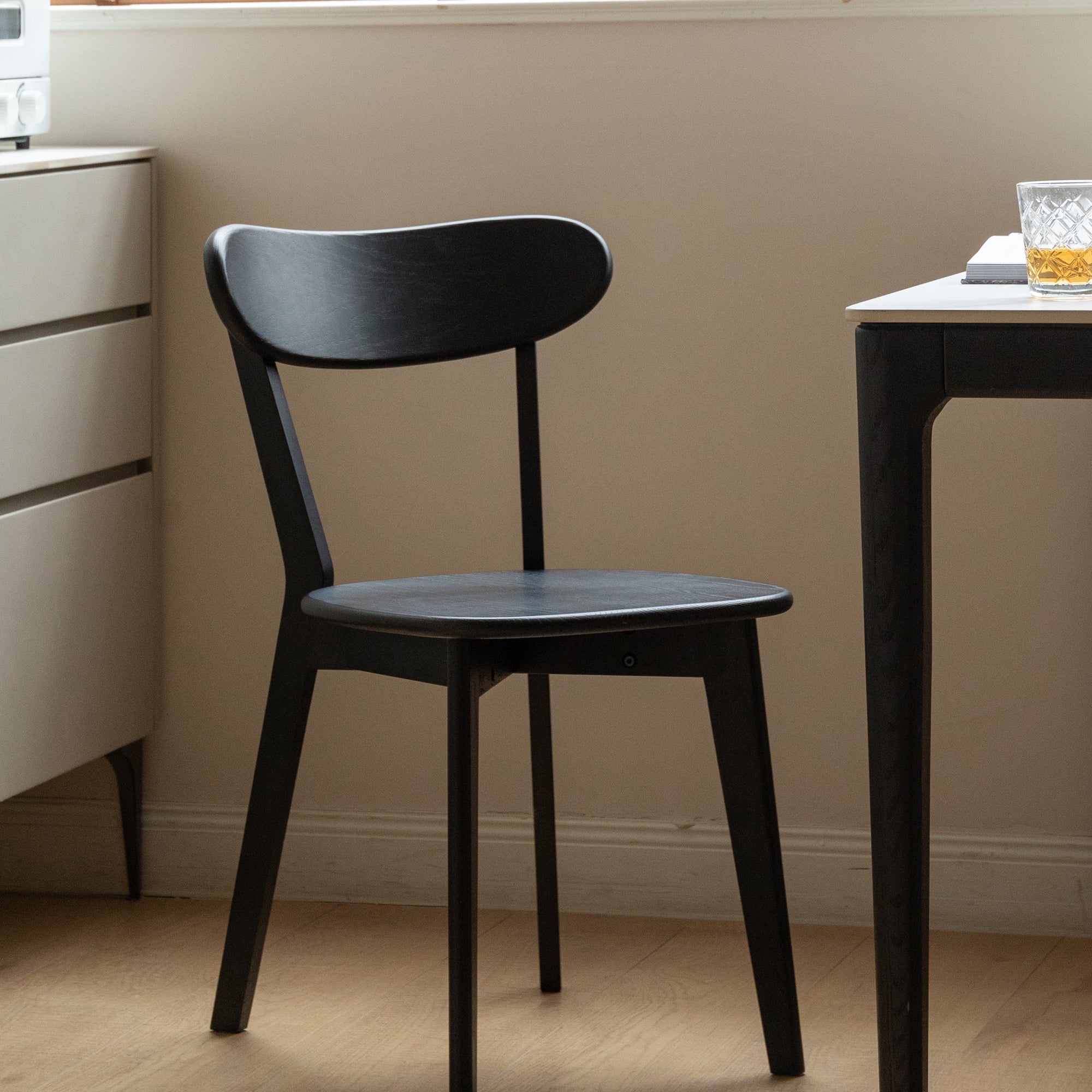 Solid Oak Dining Chair in black wood next to a dining table, blending seamlessly with minimalist home decor.