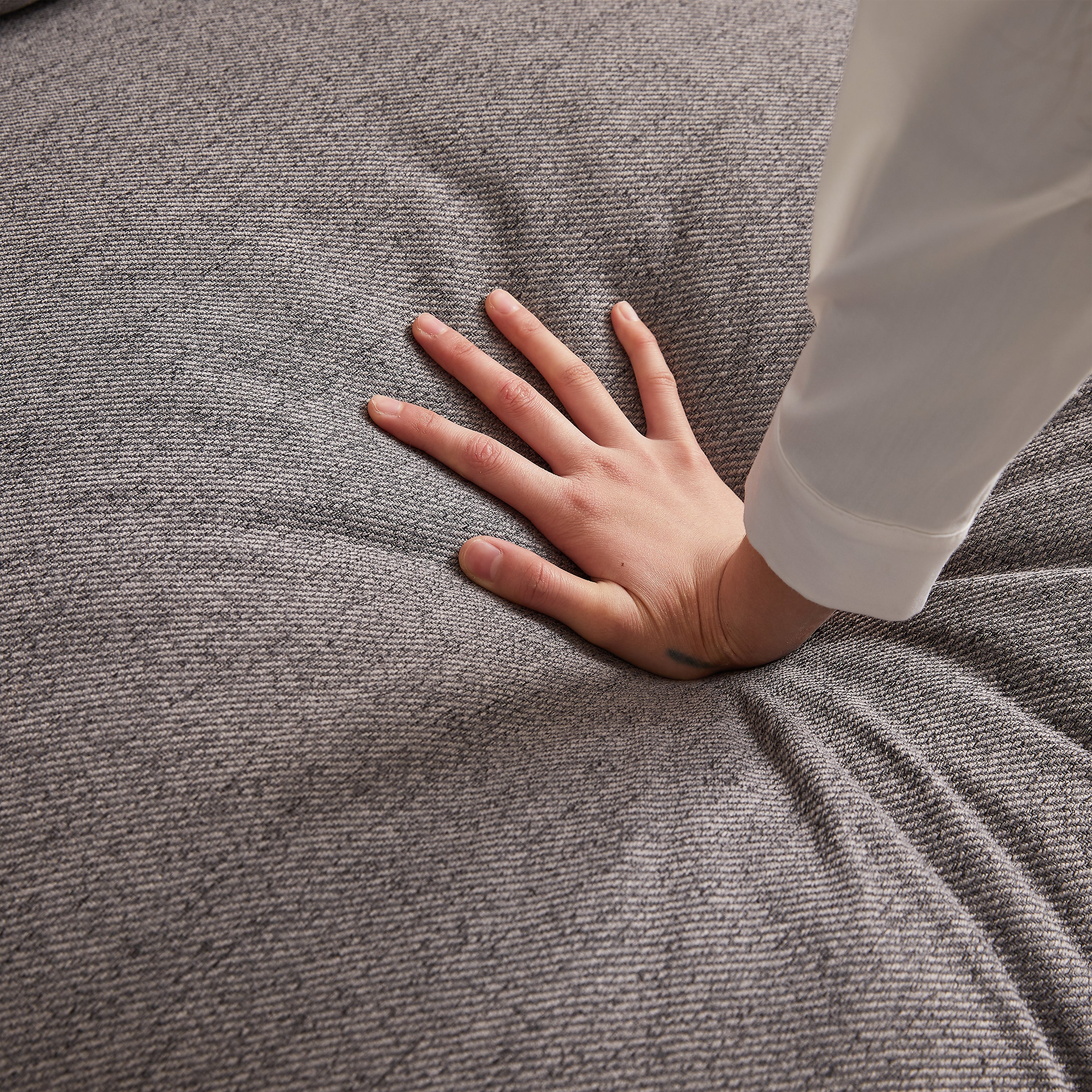 Hand pressing into cushion of modular sofa with ottoman, demonstrating the plush and supportive foam padding for maximum comfort.