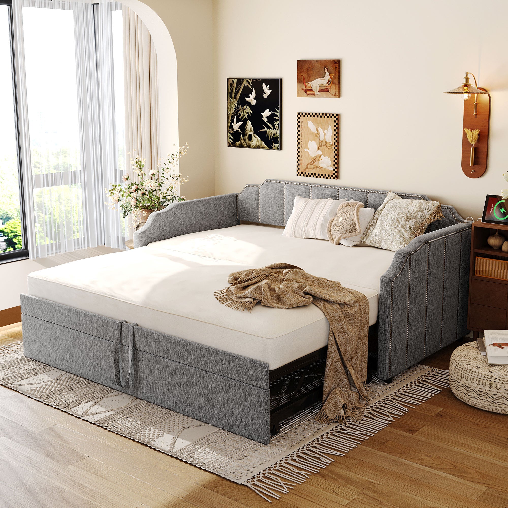 Gray upholstered twin daybed with nailhead trim, a pop-up trundle, and integrated USB charging ports in a cozy room.
