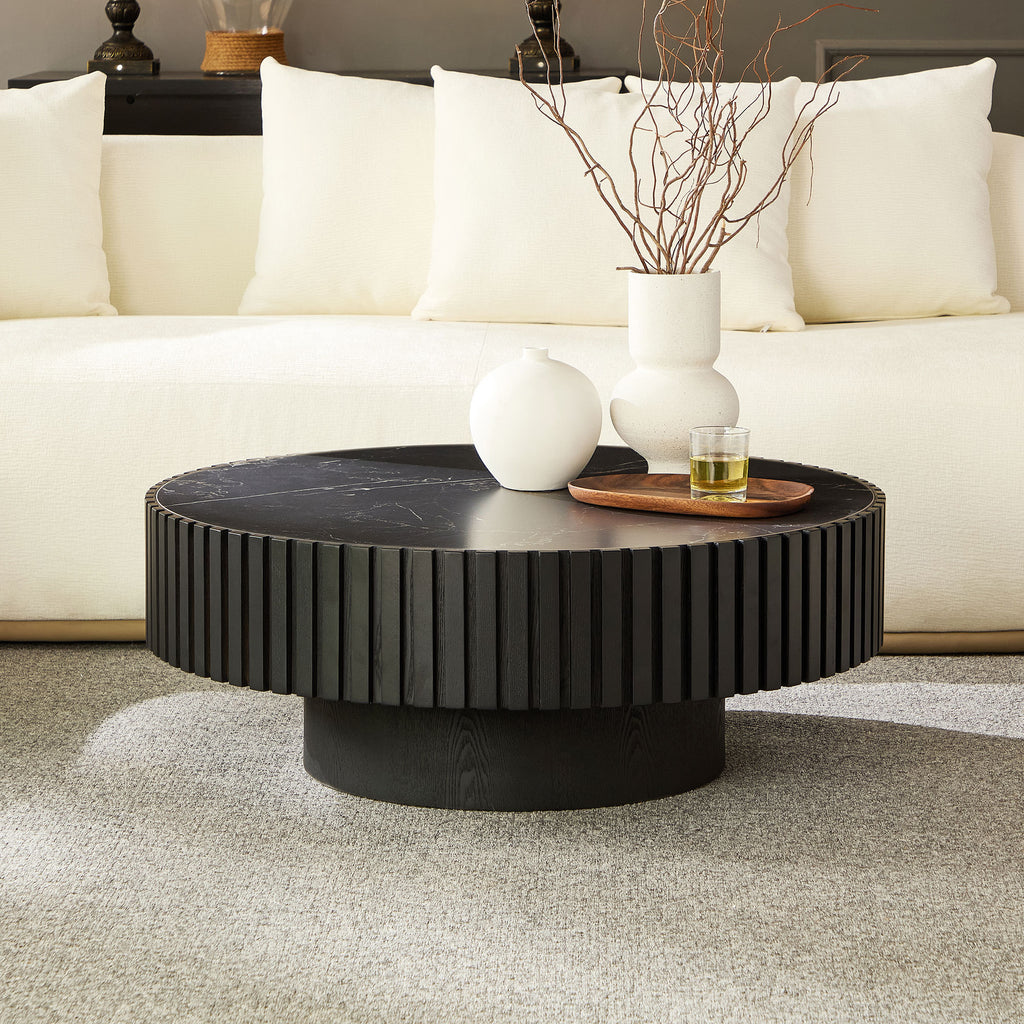 Modern black round coffee table with fluted base and sintered stone top, styled in a neutral-toned living room with white sofa.