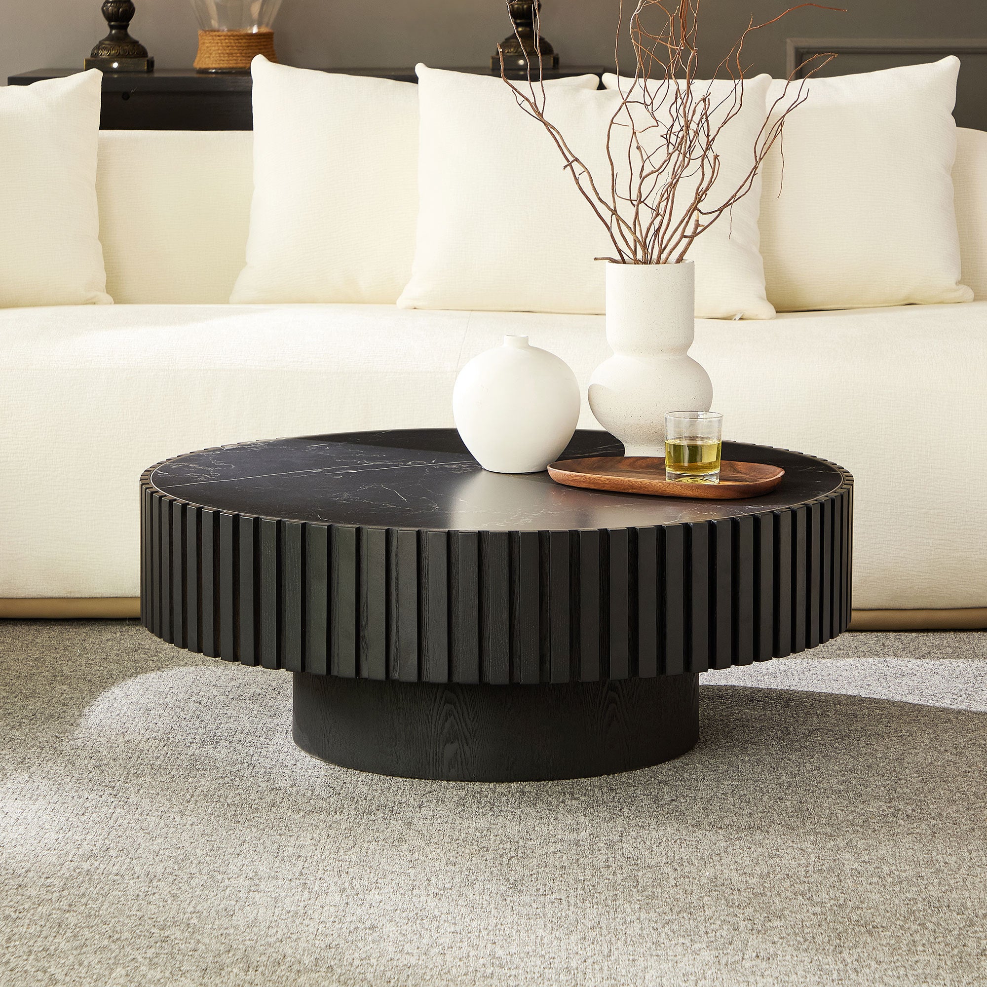Modern black round coffee table with fluted base and sintered stone top, styled in a neutral-toned living room with white sofa.