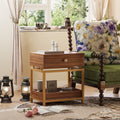 Modern walnut end table with a drawer and open shelf, featuring a sleek gold metal frame beside a floral armchair.