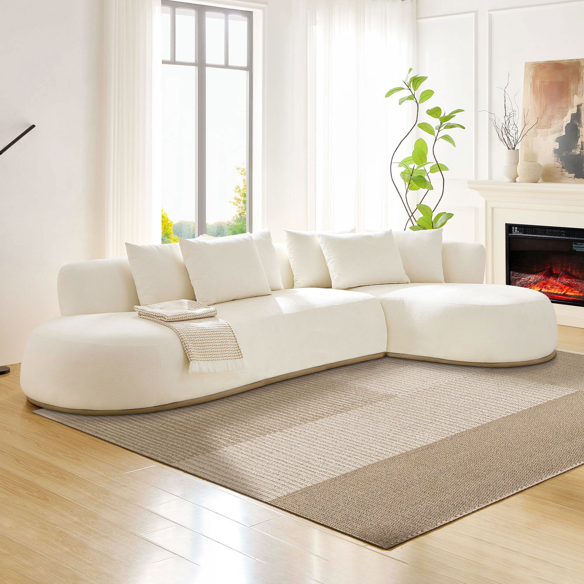 Modern oversized L-shape sectional sofa with right-facing chaise in beige, placed in a bright living room with fireplace and large windows.