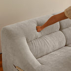Hand pressing into backrest of beige memory foam sofa, demonstrating plush support and comfort of the compact 2-seater design.