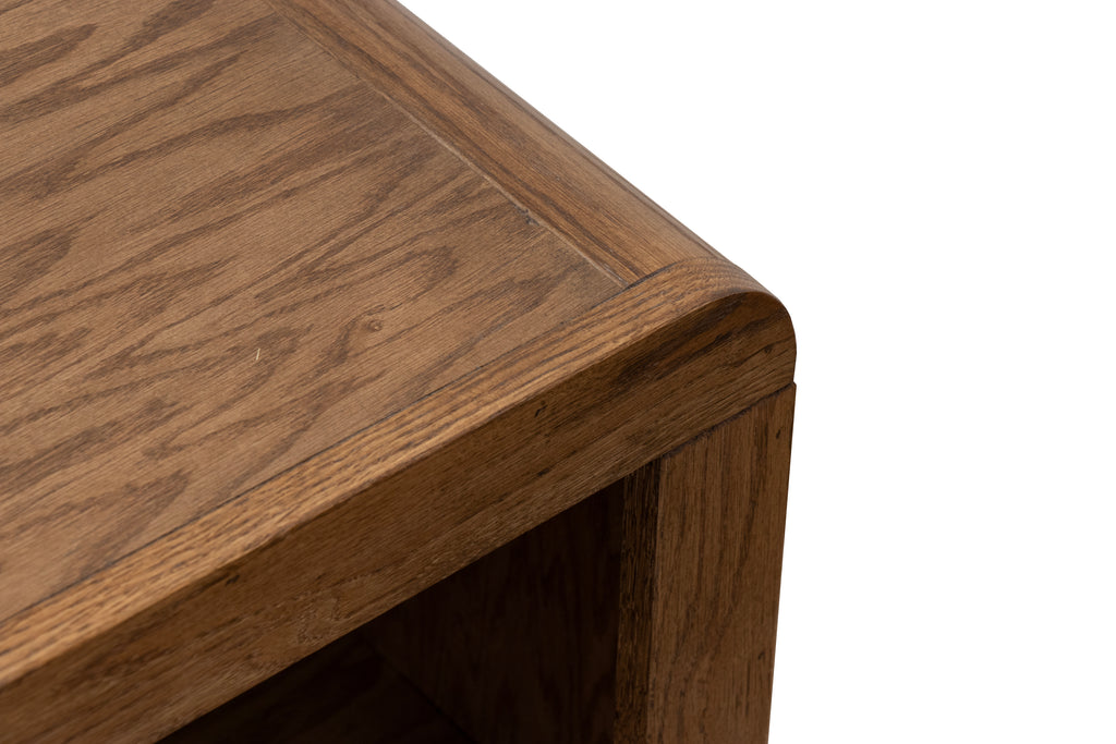 Close-up of Haven Oak Coffee Table corner, displaying smooth curved edge and rich bourbon finish on oak wood grain.