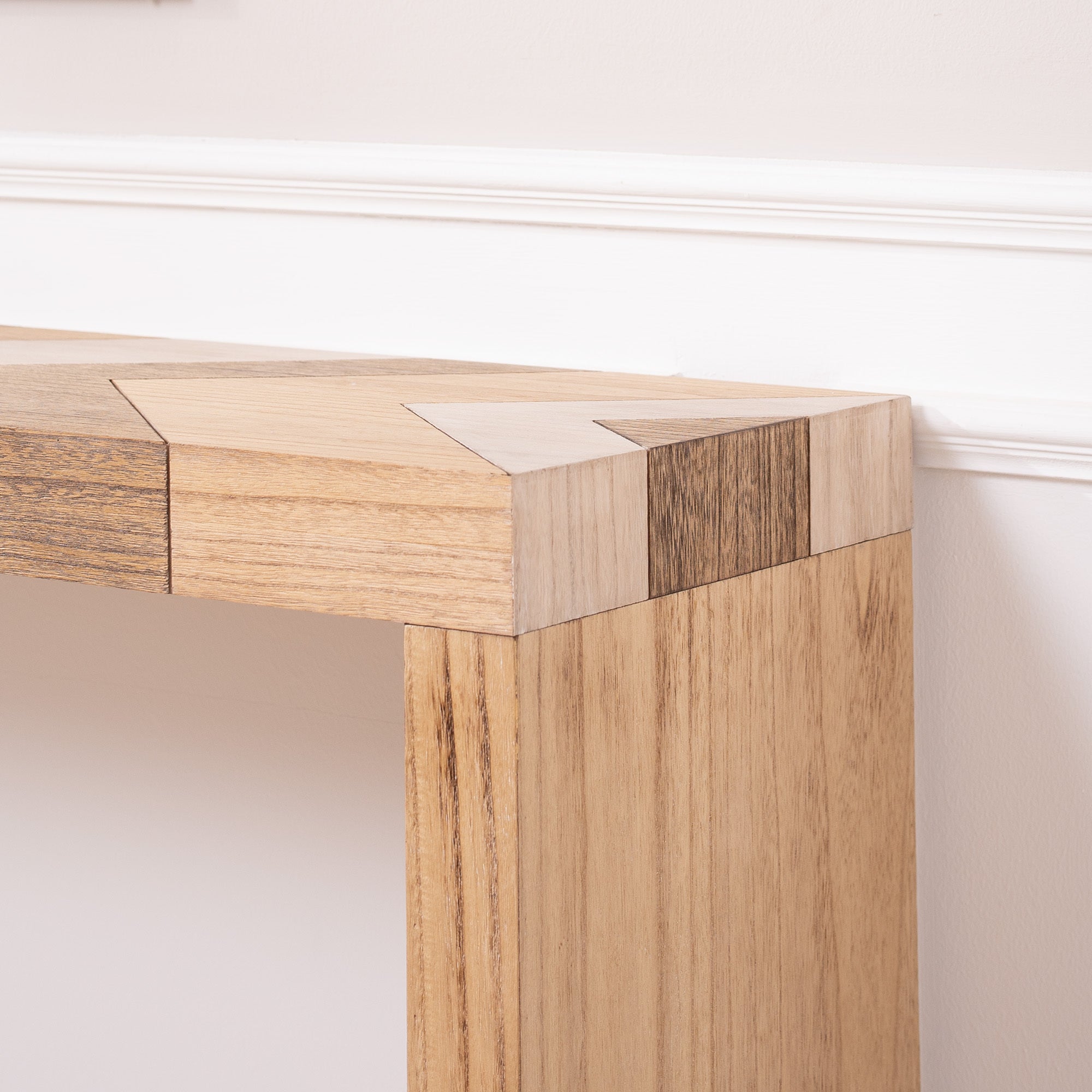 Corner detail of modern console table with chevron top, showcasing precise joinery and wood tone variation.