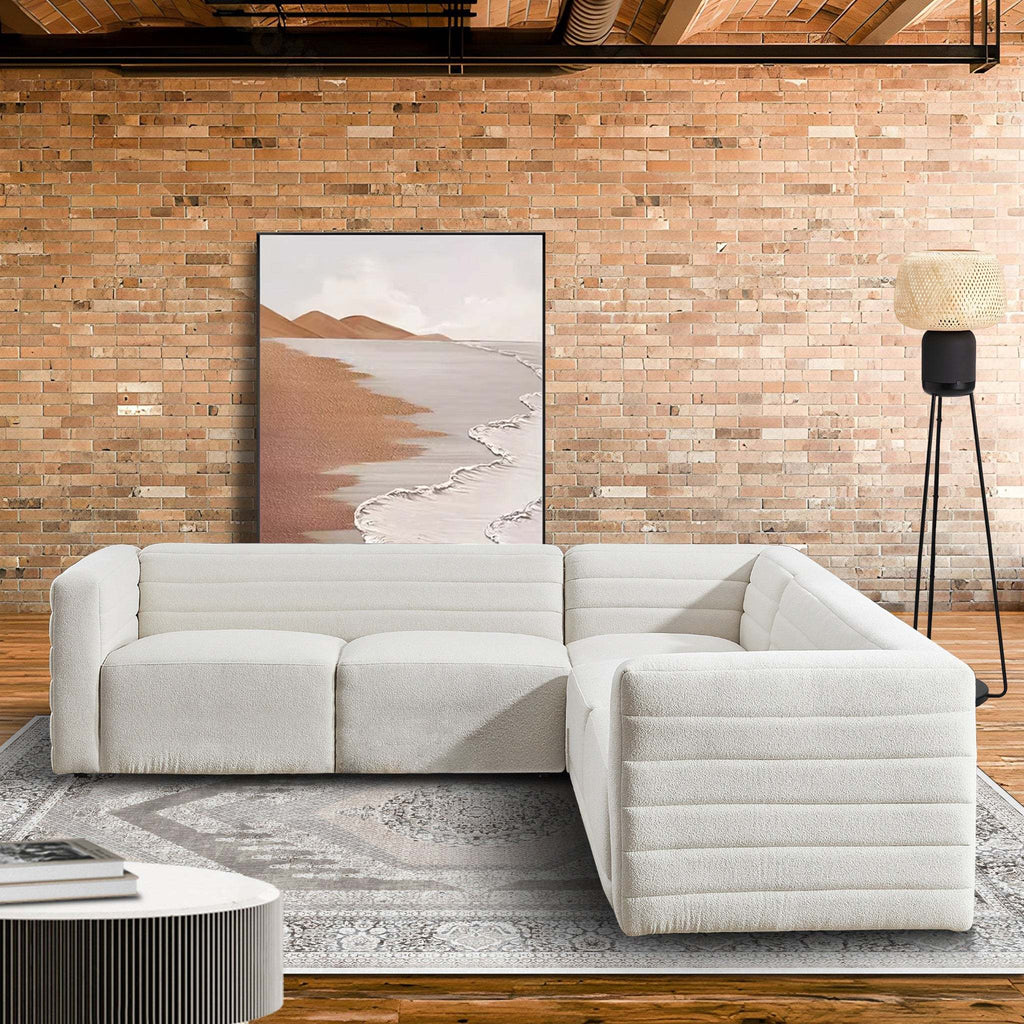 Cream boucle corner sectional sofa with a modern, channel-tufted low profile design in a rustic brick-wall living room.