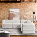 Cream boucle corner sectional sofa with a modern, channel-tufted low profile design in a rustic brick-wall living room.