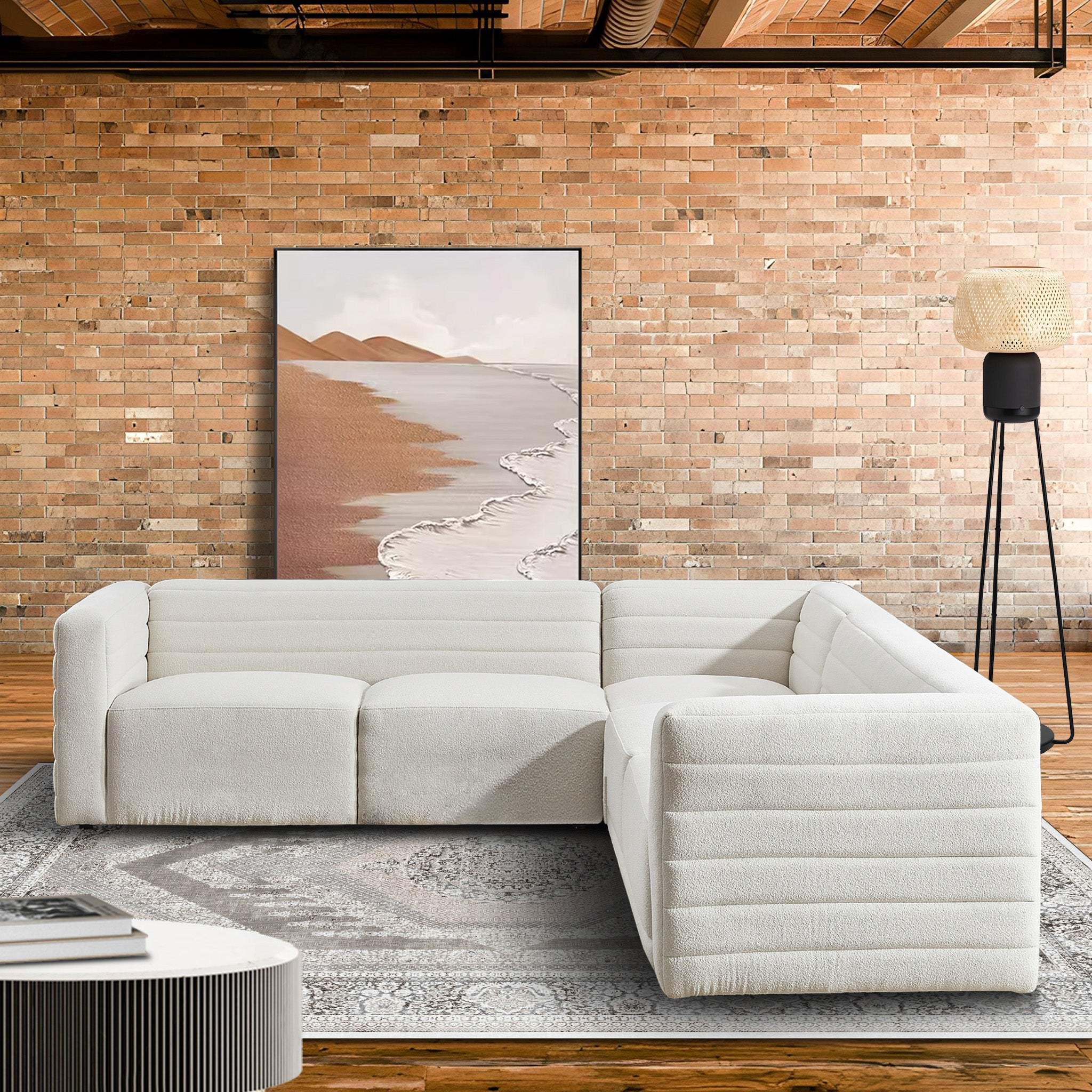 Cream boucle corner sectional sofa with a modern, channel-tufted low profile design in a rustic brick-wall living room.