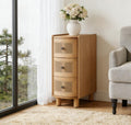 Light oak nightstand with three rounded cane-front drawers, standing on short cylindrical legs in a bright room.