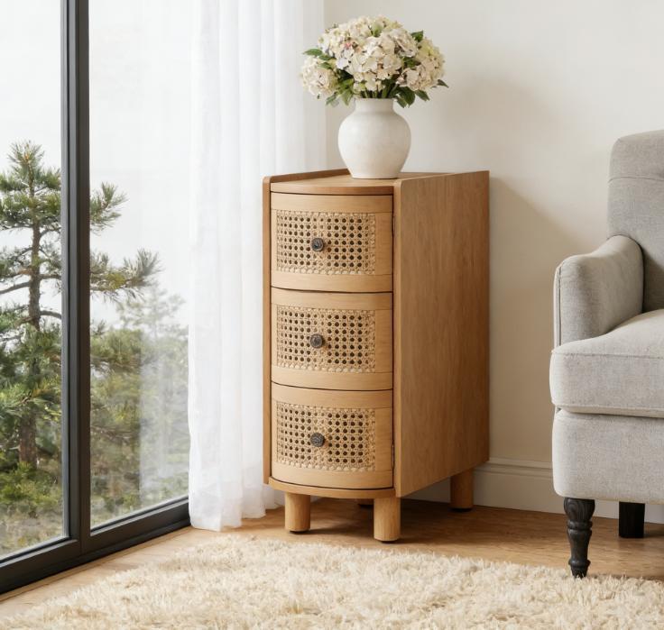 Light oak nightstand with three rounded cane-front drawers, standing on short cylindrical legs in a bright room.