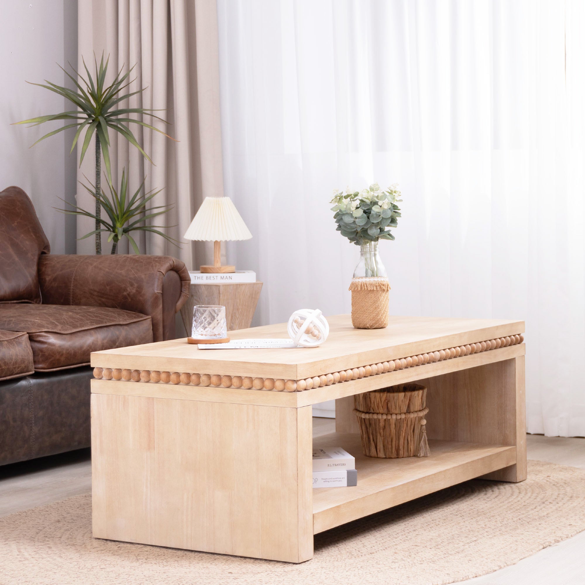 Light natural wood coffee table with open shelf and beaded trim placed in a bright living room with neutral decor.