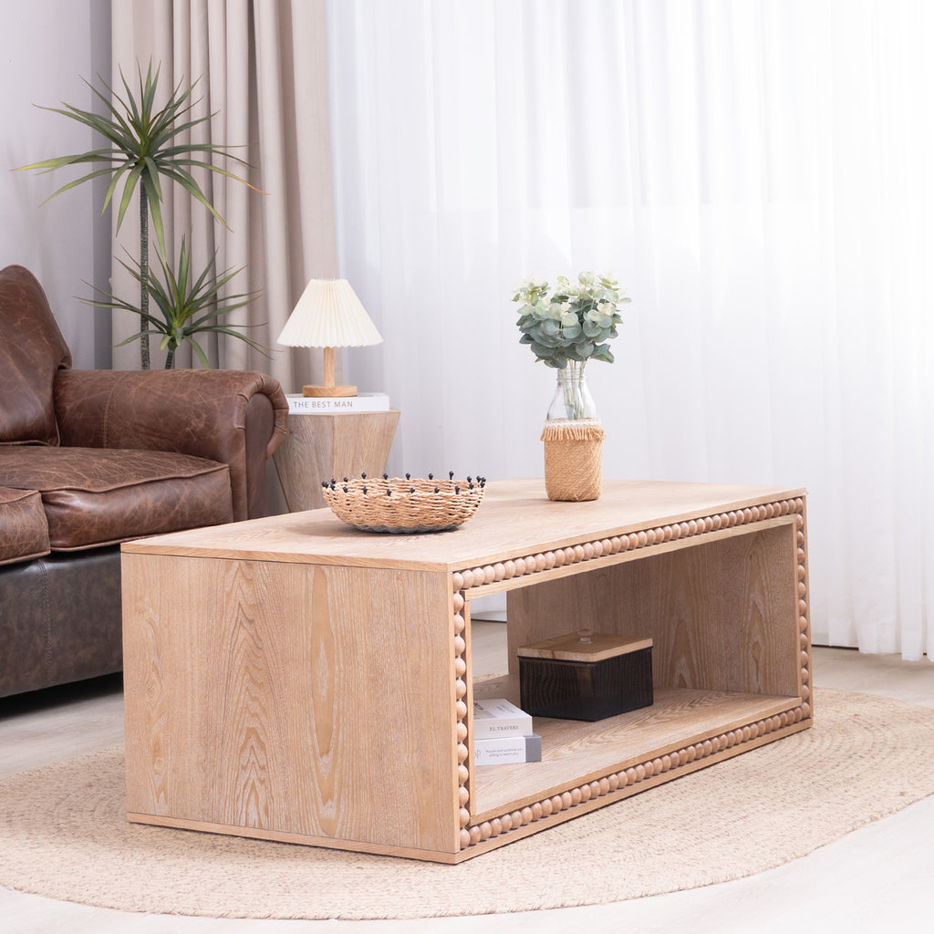 Modern farmhouse coffee table with natural wood finish, styled with decor on top and books on the open shelf in a bright room.