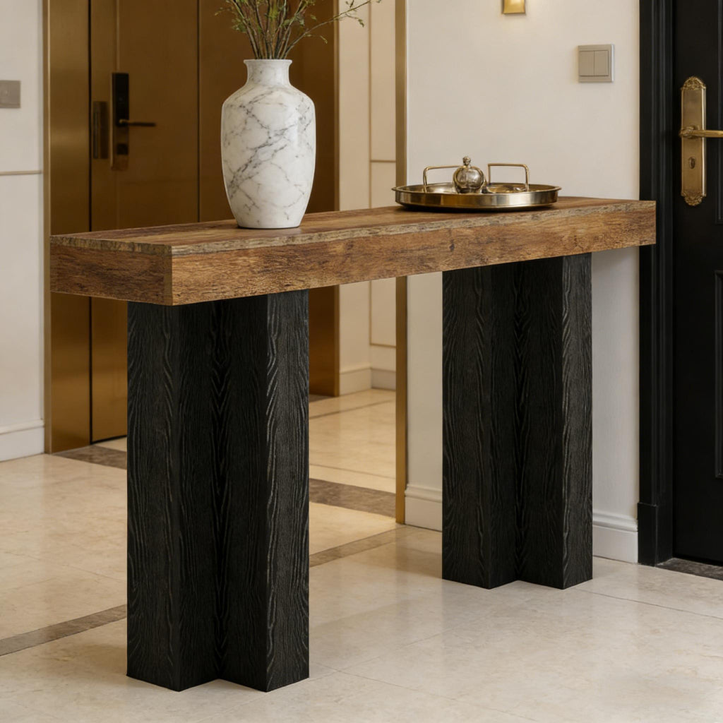 Modern narrow console table with a thick wood-grain top and bold, black textured pedestal legs in a luxe entryway.