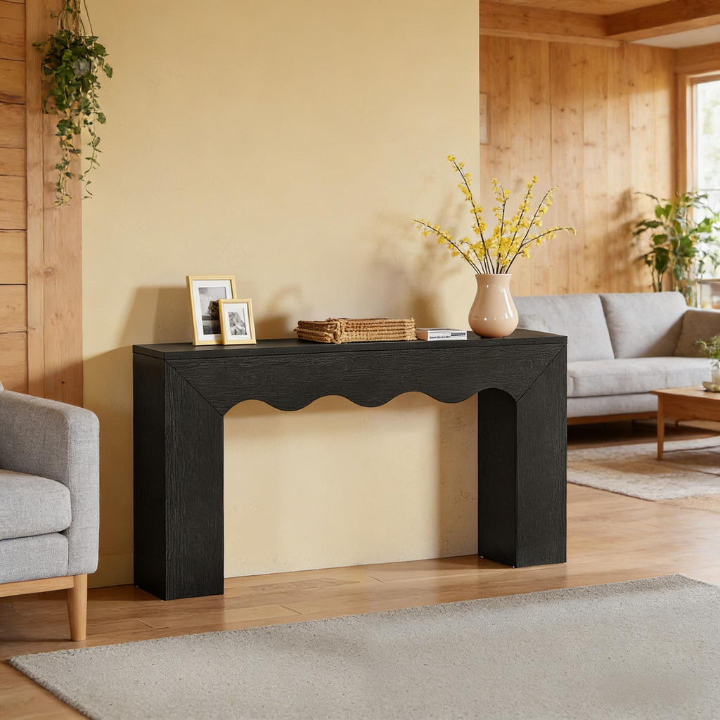 Modern black wood console table with a minimalist frame and a distinctive scalloped, wavy edge apron.