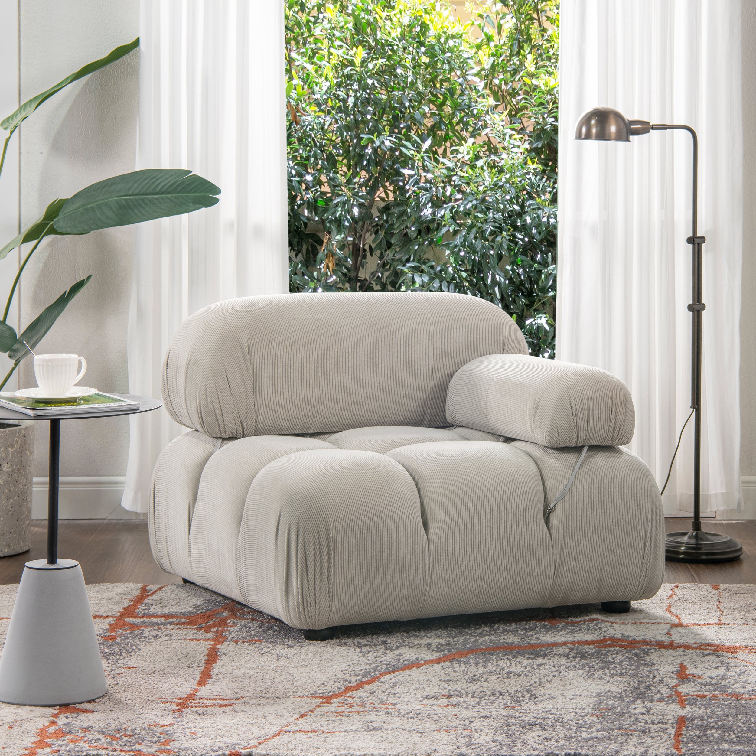 Modern gray lounge arm chair in pebble corduroy with modular bubble design, placed in a bright living room with floor lamp and rug.