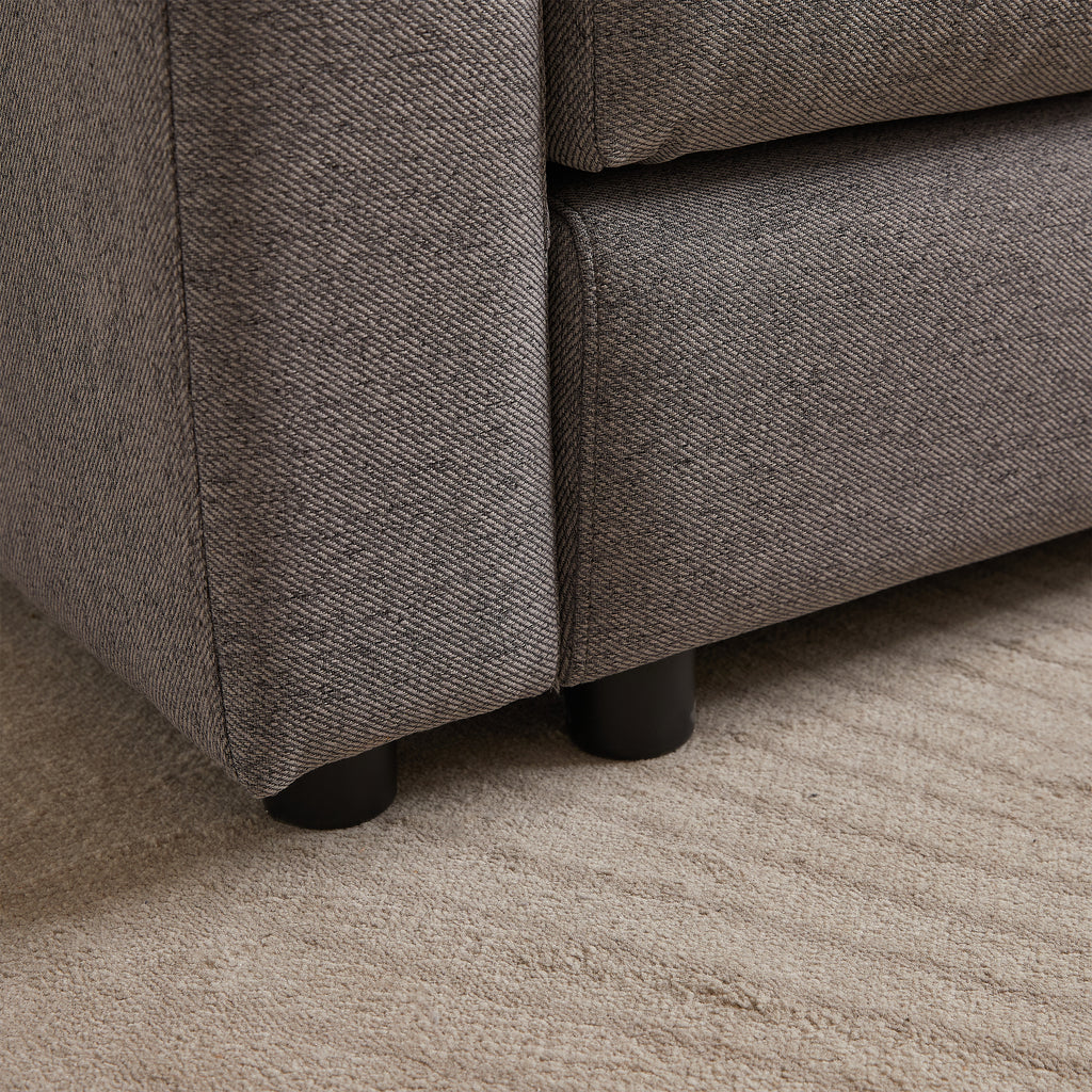 Close-up of sofa leg and fabric texture on modular sofa with ottoman, showing sturdy black legs and durable upholstery.