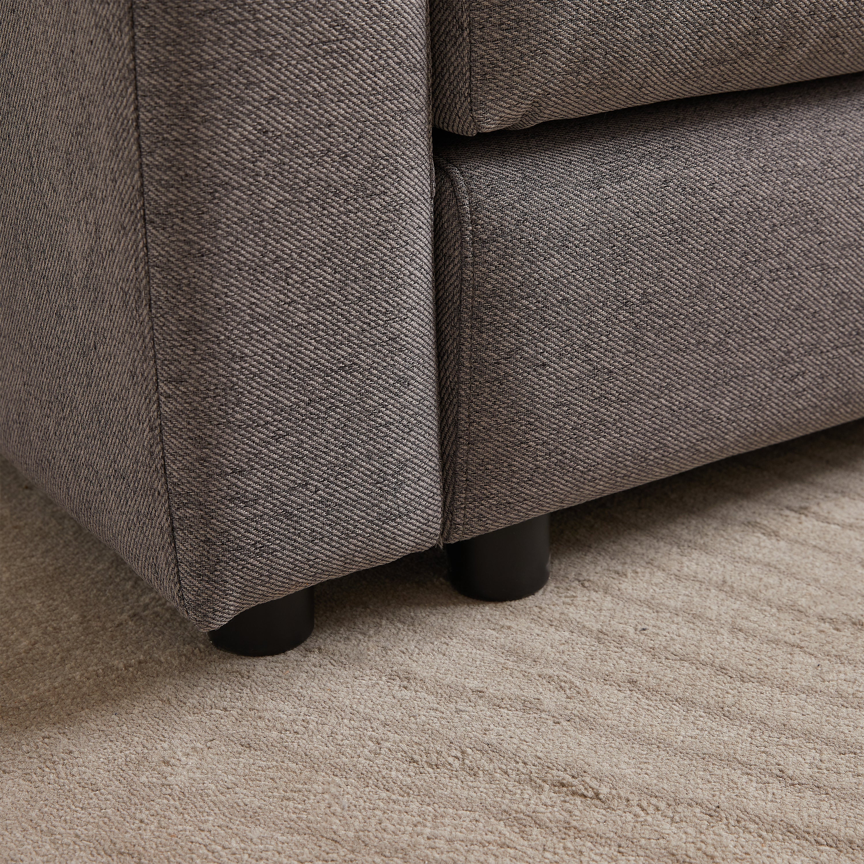 Close-up of sofa leg and fabric texture on modular sofa with ottoman, showing sturdy black legs and durable upholstery.
