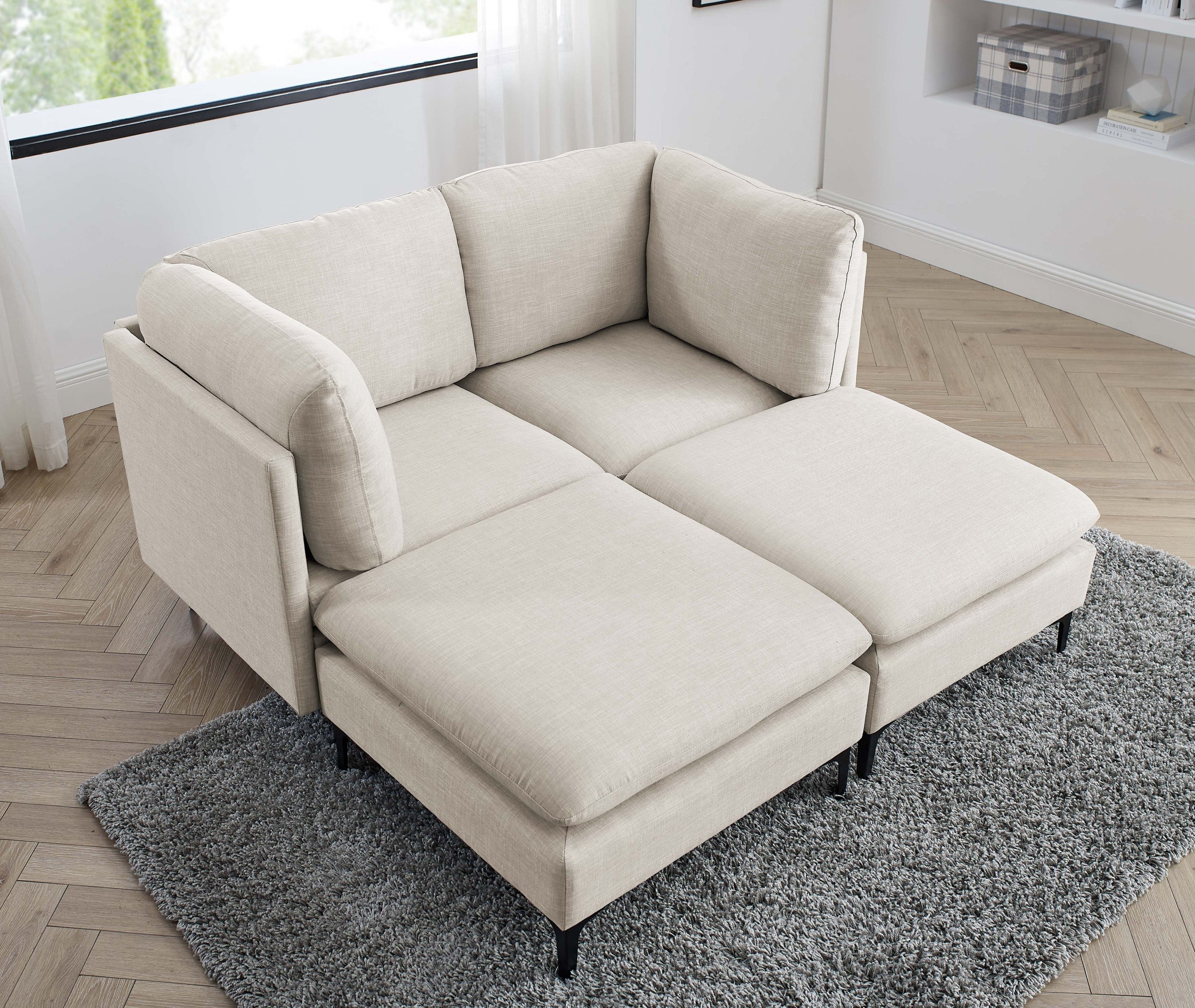 Modern beige linen modular sectional sofa with plush cushions and slim black metal legs on a grey shag rug.