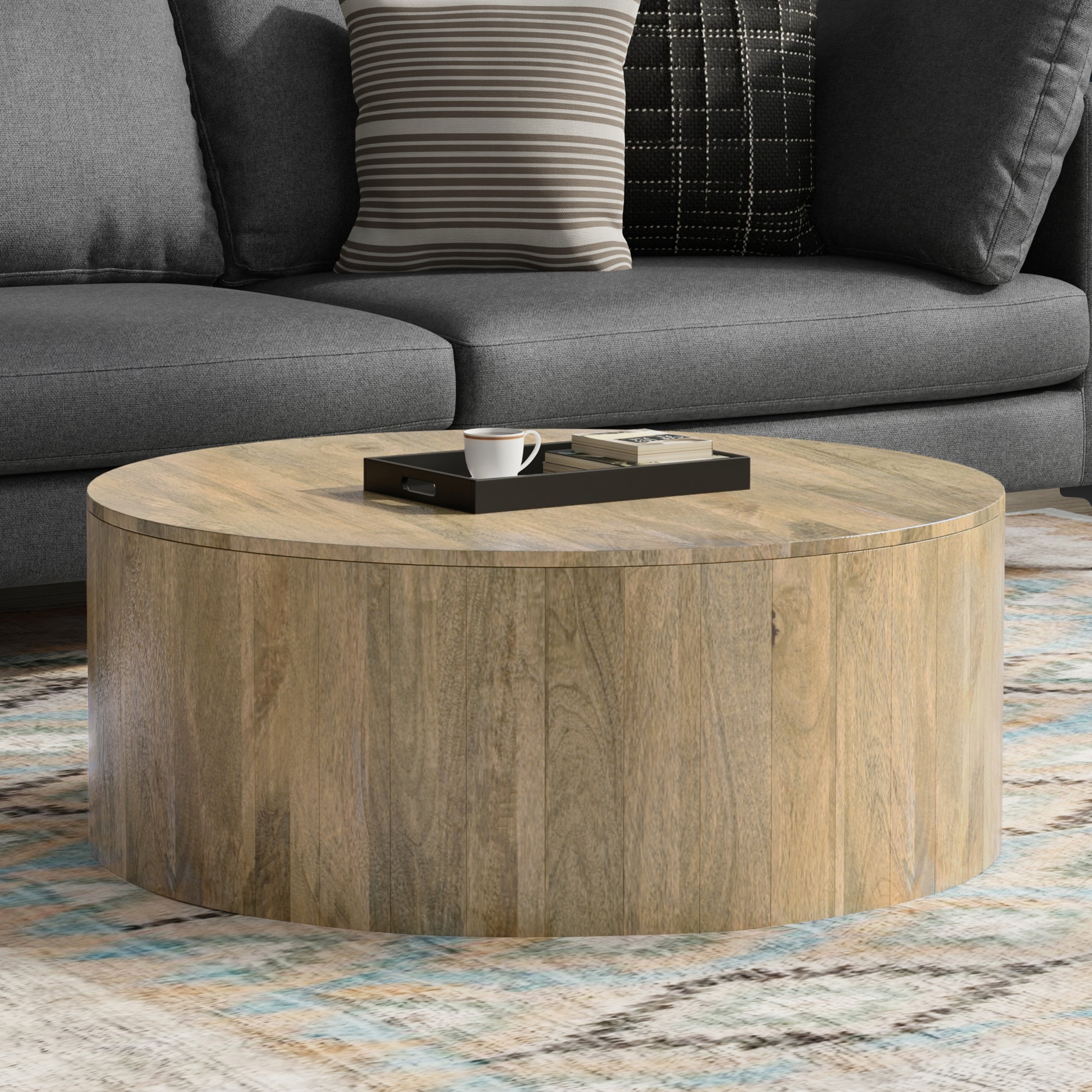 Millbury Drum Coffee Table in wood placed in a modern living room, showcasing its spacious, multi-functional design and natural mango wood finish.