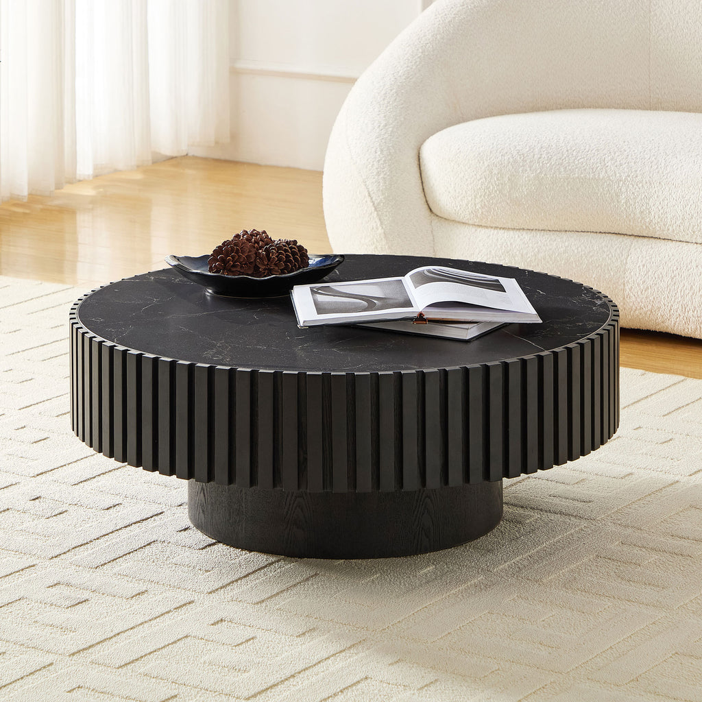 Black sintered stone coffee table with fluted base, placed in a bright room with curved white sofa and light wood flooring.