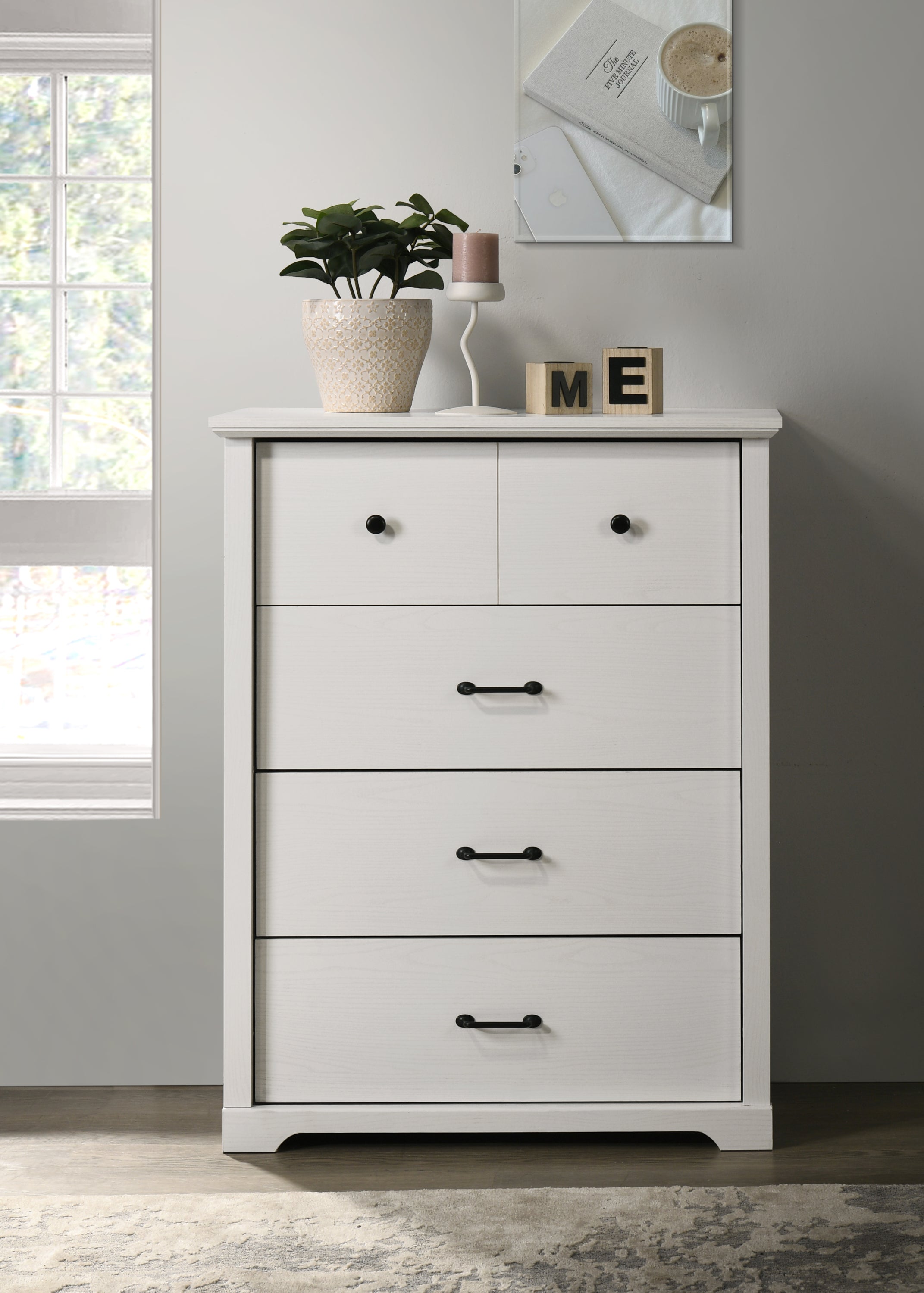 Elara White 4-Drawer Chest with black metal handles in a modern bedroom setting. Features sleek white wood finish and compact 32-inch width.