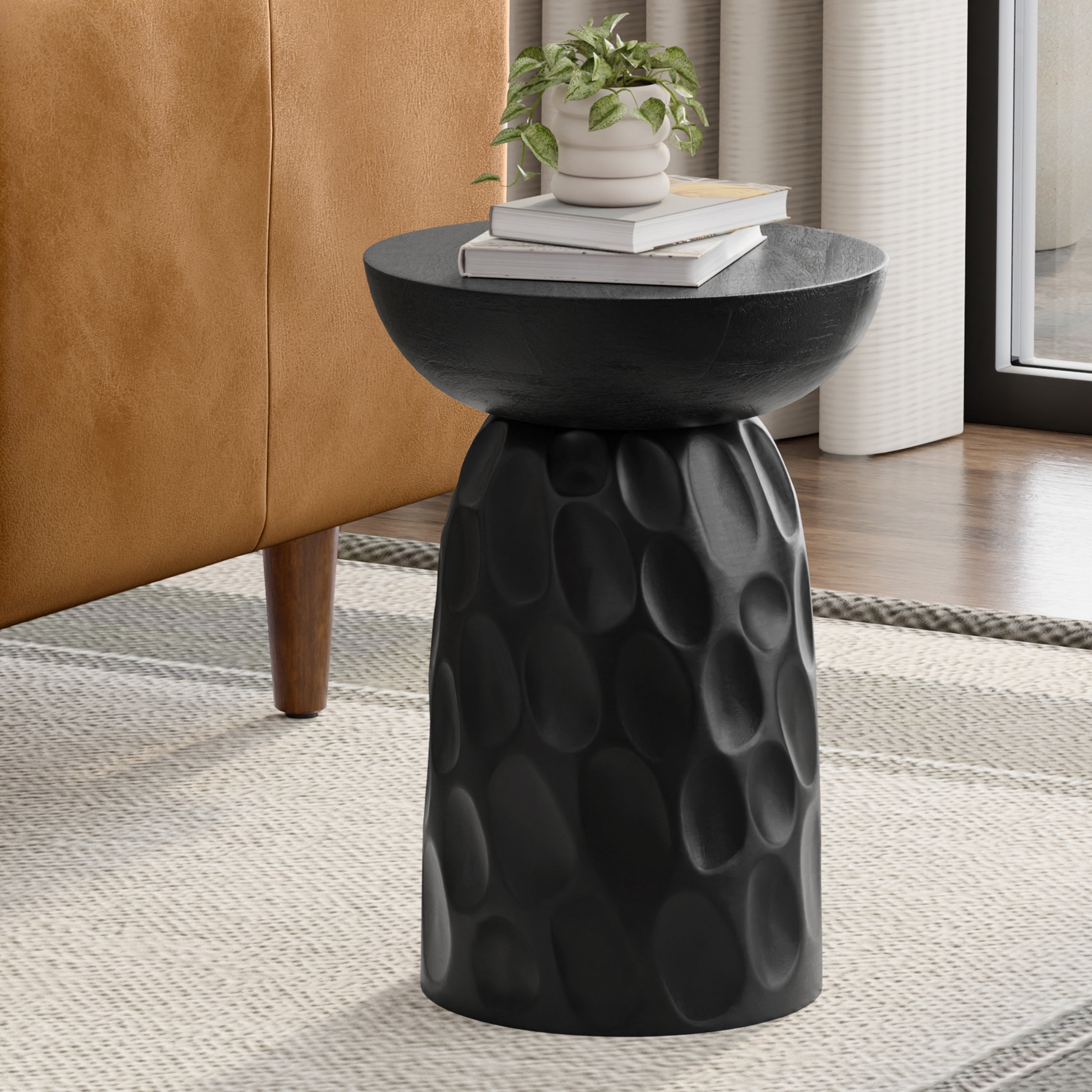 Black round accent table made of solid mango wood, featuring a textured, carved pedestal base and a smooth top.