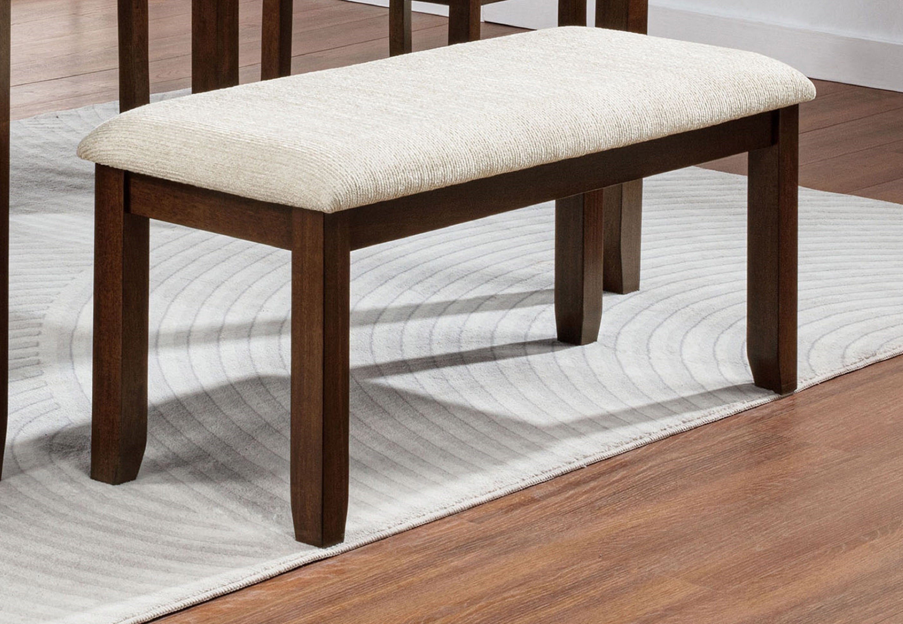 Contemporary Wood Finish Dining Bench placed on a light rug in a dining room, showcasing its modern design and beige fabric seat.