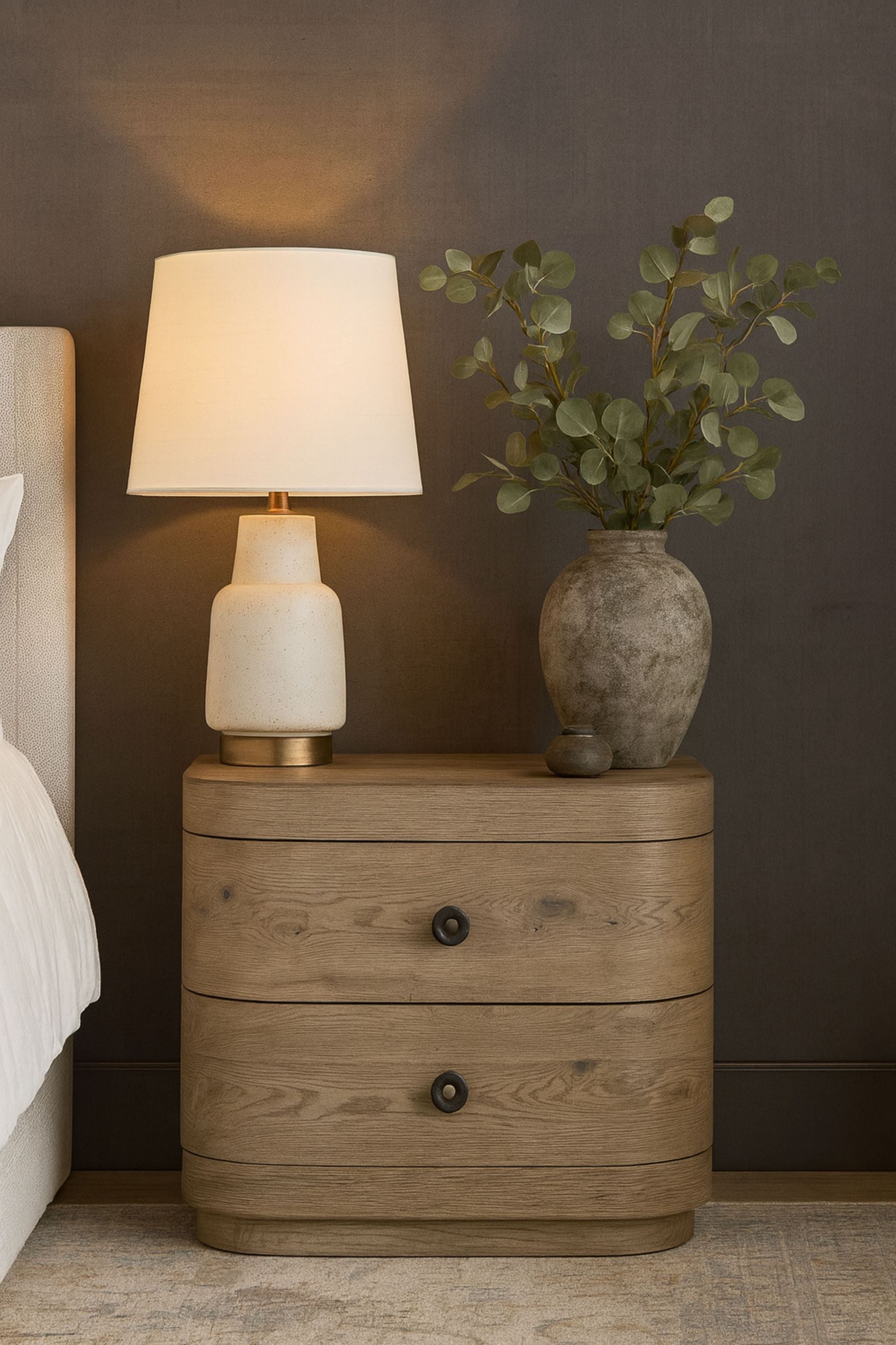2-Drawer Oak Nightstand with USB styled in a bedroom, topped with a lamp and vase, showcasing its elegant knotty oak veneer and curved design.